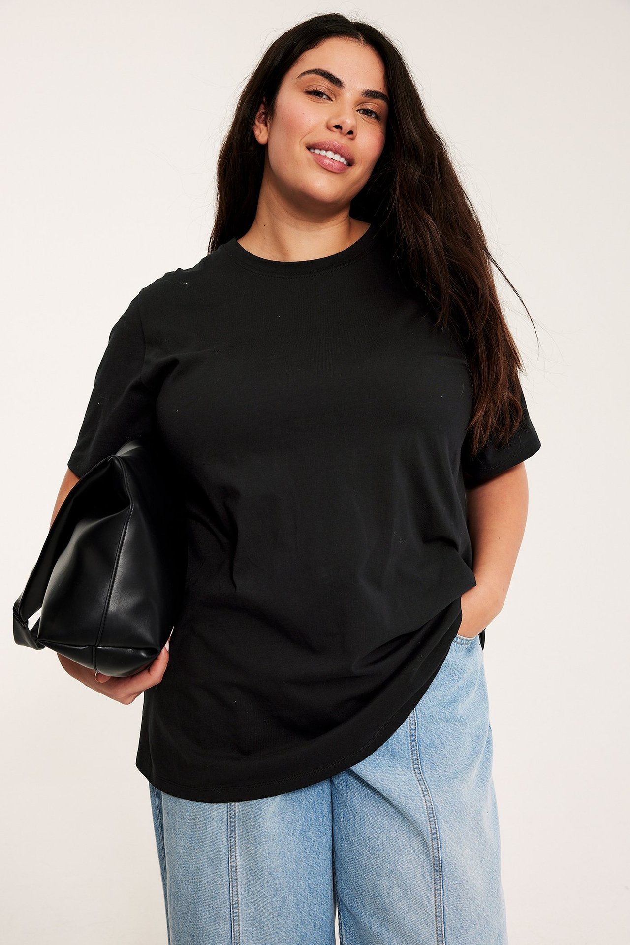 Kvinne i svart lang bomulls-t-skjorte, lyseblå jeans, holder en svart håndveske.