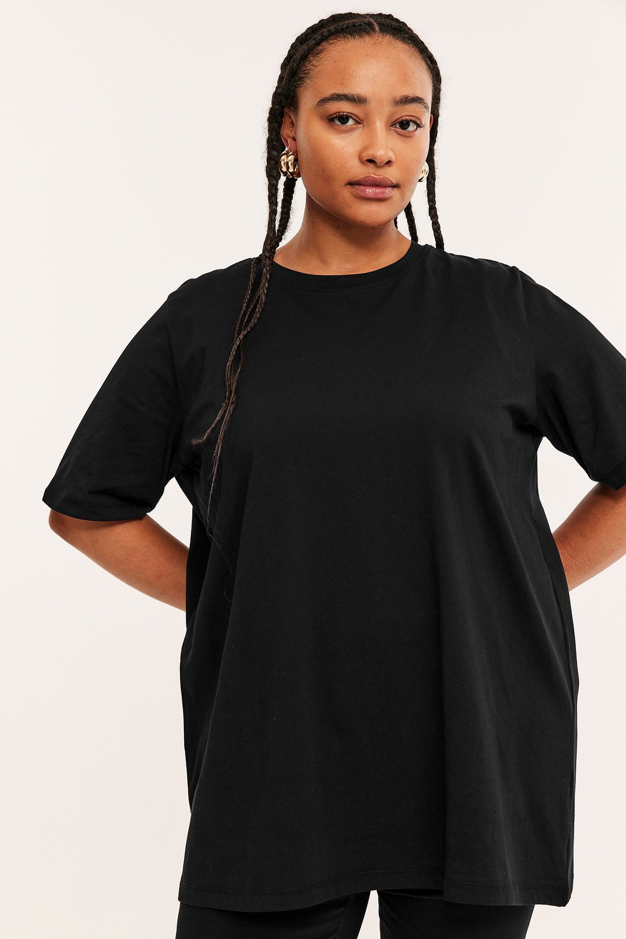 Framifrån, kvinna i svart, lös lång bomulls-t-shirt tunika och guldiga ringörhängen.