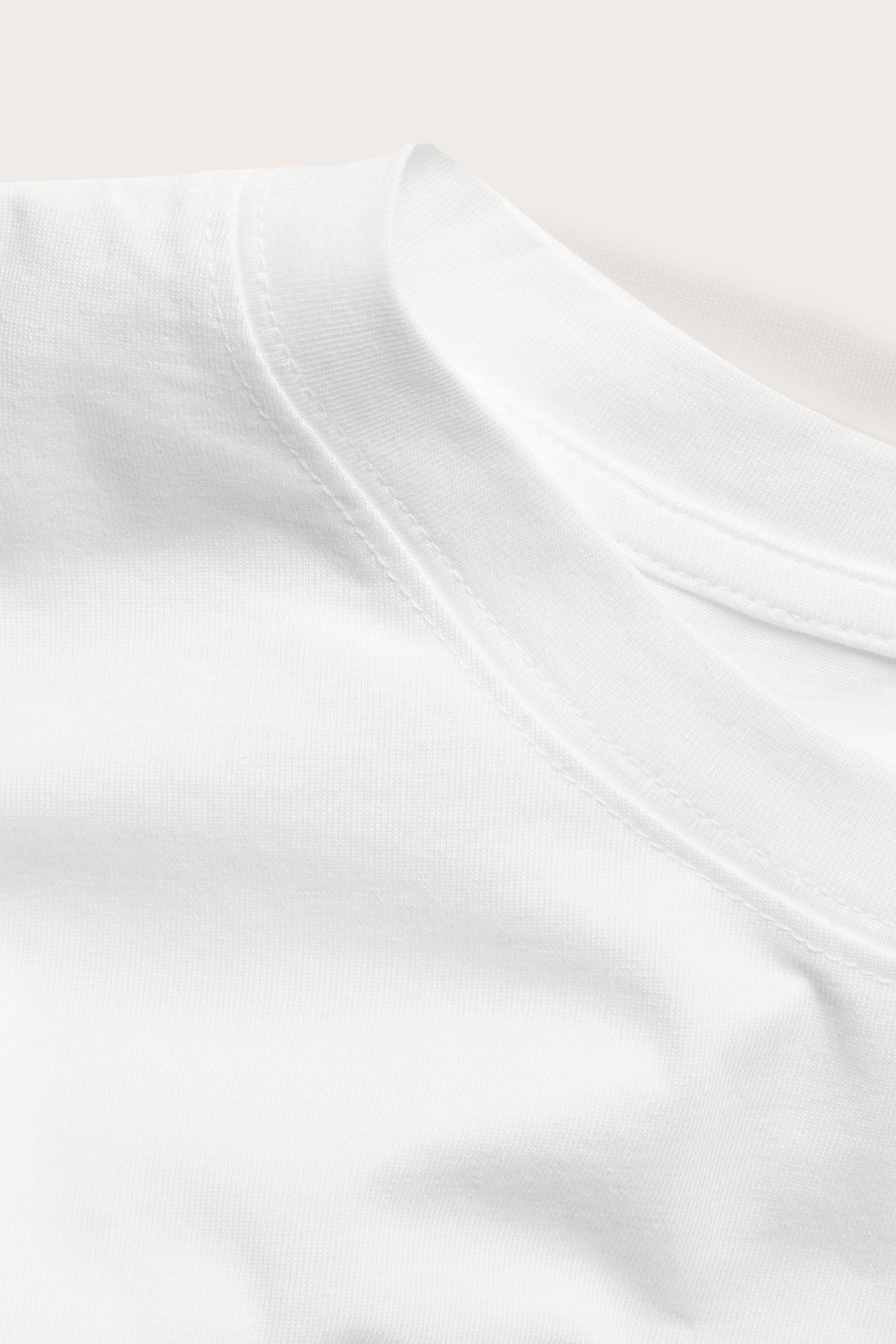Zbliżenie na gładki biały bawełniany t-shirt z prążkowanym okrągłym dekoltem i szwem na ramieniu.