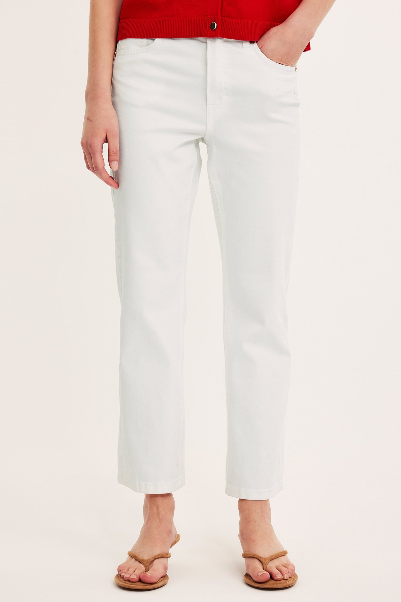 Frontvy av en kvinna i vita croppade flare jeans, en röd topp och bruna flip-flop sandaler.