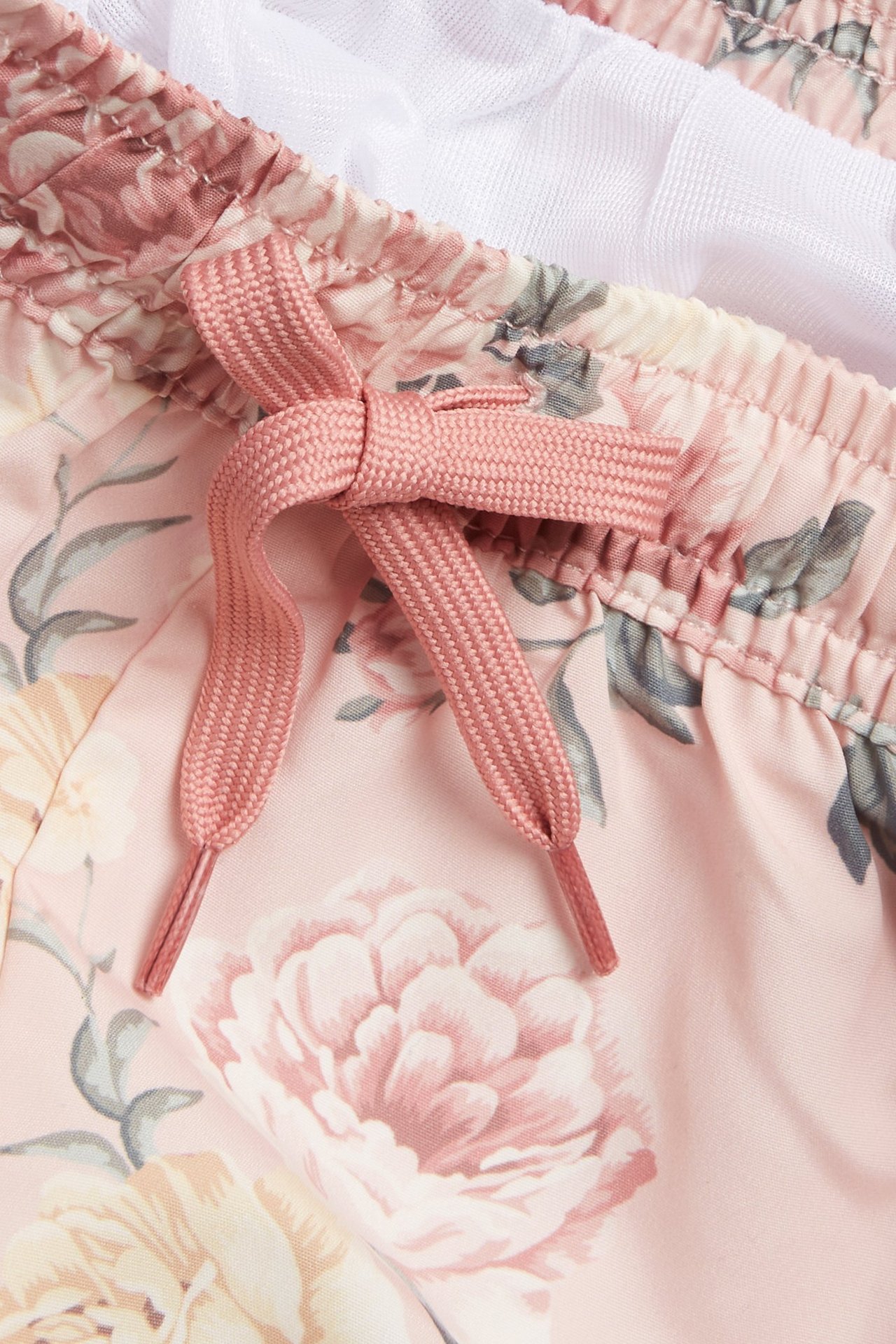 Lähikuva vaaleanpunaisista kukkakuvioisista vauvan/lasten uimashortseista, joissa on kiristysnyöri ja valkoinen verkkovuori.