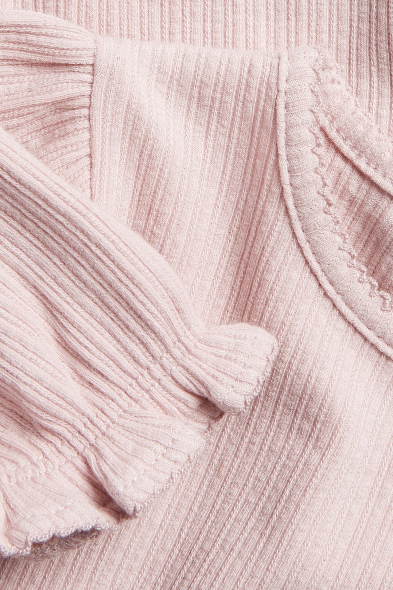 Närbild av en rosa ribbad jersey babybody med korta puffärmar och picotkant.