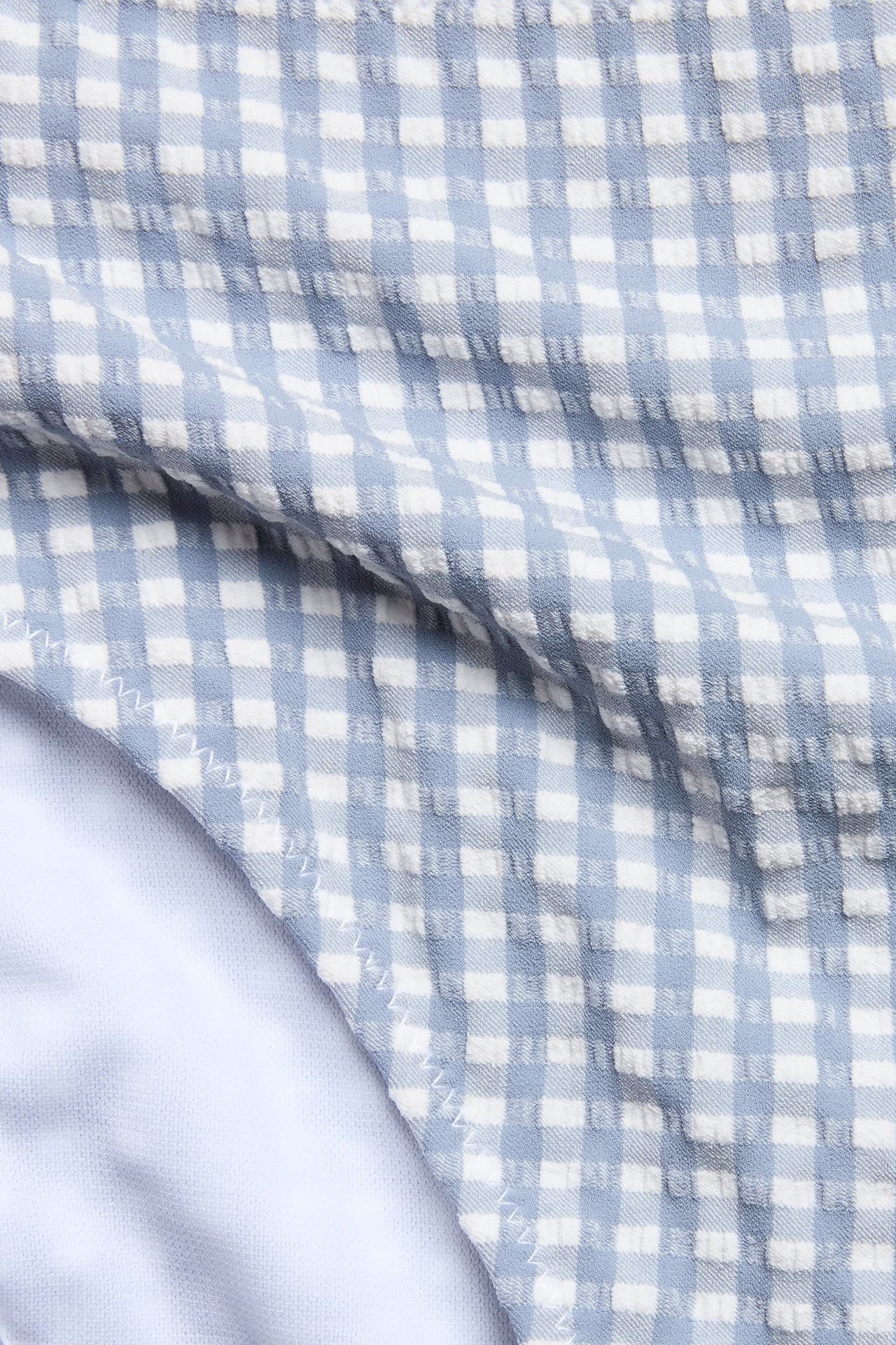 Zbliżenie damskich spodenek bikini z wysokim stanem, niebiesko-białych w kratkę, z teksturowanego materiału i białą podszewką.