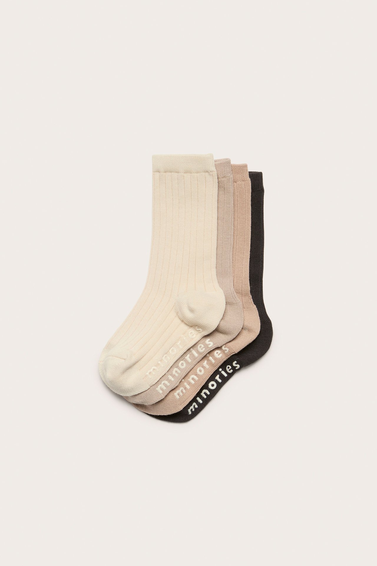 Ylhäältä: Neljä ribbineulottua lastensukkaa: beige, vaaleanruskea, keskiruskea, musta, liukuestetekstillä 'minories'.