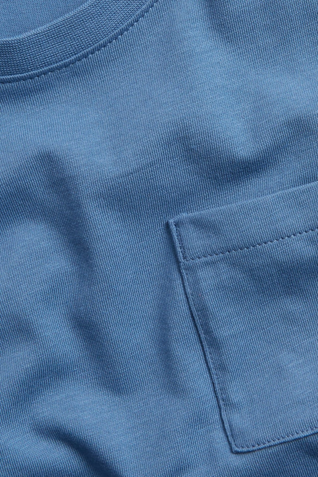 Zbliżenie niebieskiej bawełnianej koszulki z długim rękawem, z prążkowanym dekoltem i kieszonką na piersi.