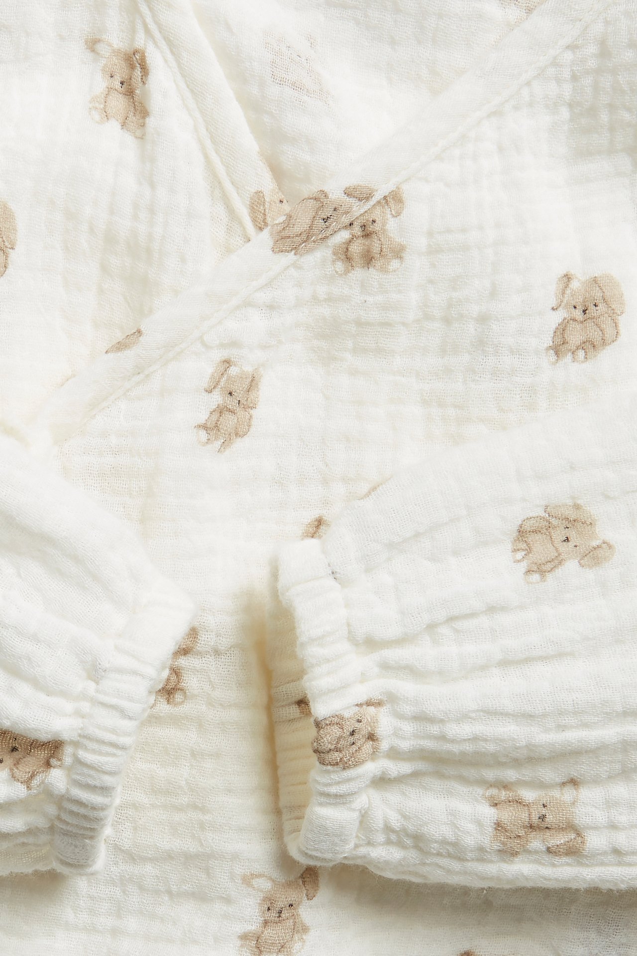 Lähikuva offwhite-värisestä vauvan kietaisubodysta, jossa on kuviollinen puuvillamusliini ja pupupainatus.