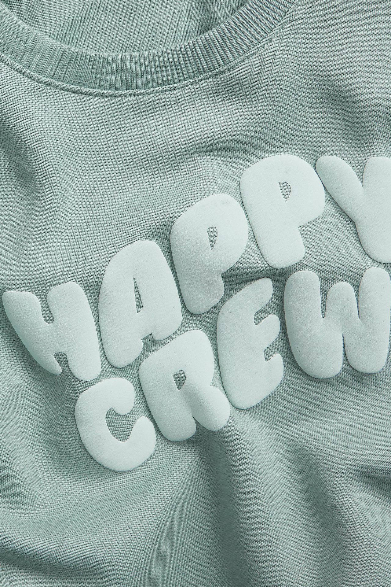 Zbliżenie z przodu na jasnozieloną bluzę z wypukłym nadrukiem "HAPPY CREW".
