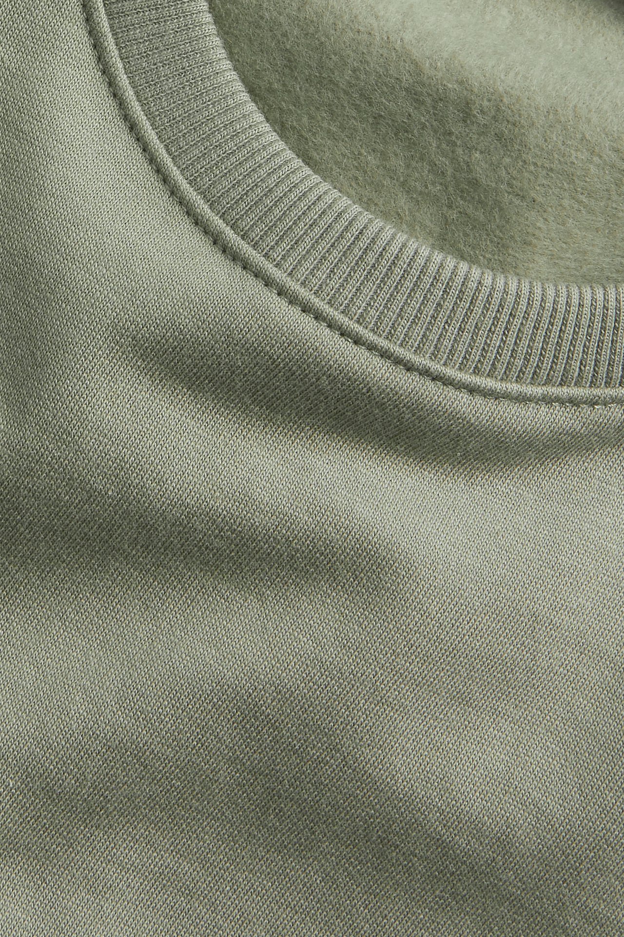 Närbild på en enfärgad grön bomullssweatshirt med ribbad rundhals.
