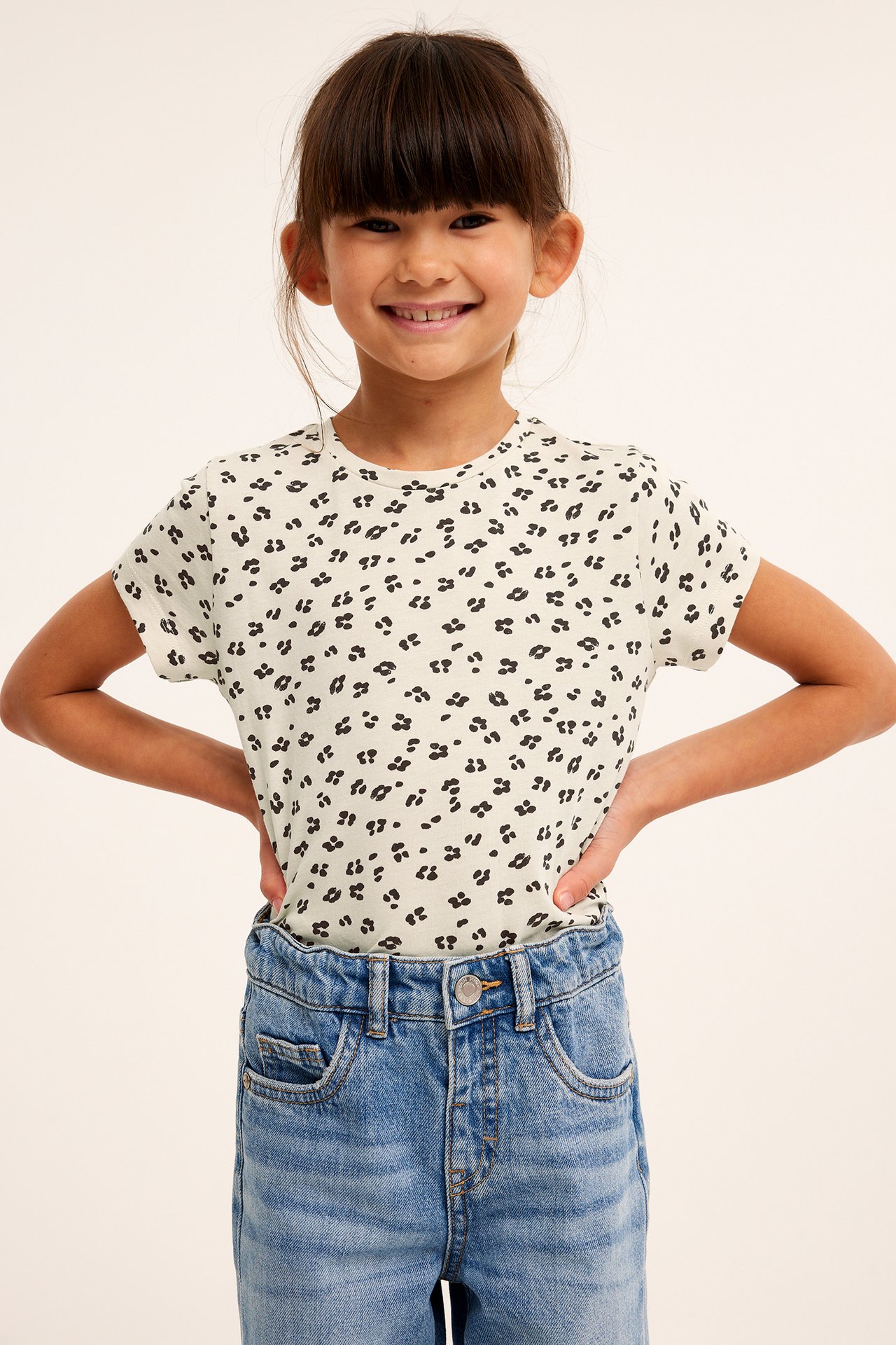 Framifrån: Ett barn i beige leopardmönstrad bomulls-t-shirt och blå jeans.