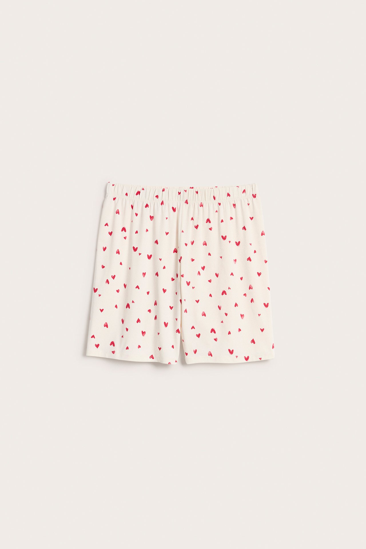 Framsida av offwhite bomullsblandning shorts med resår i midjan och rött hjärtmönster.