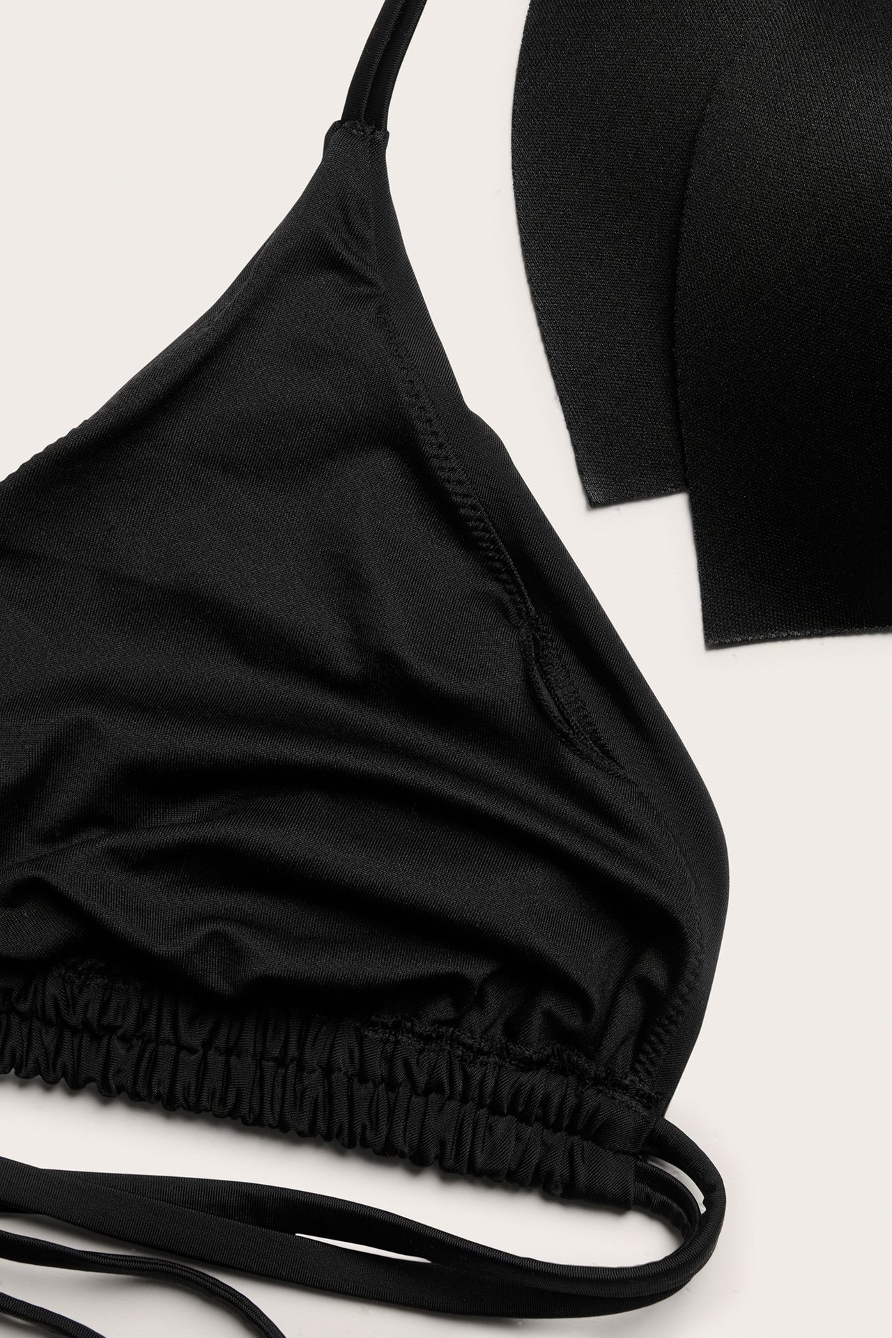 Nærbilde av en svart ensfarget trekant-bikinitopp med tynne stropper og rynket nederkant, med uttakbar vattering.