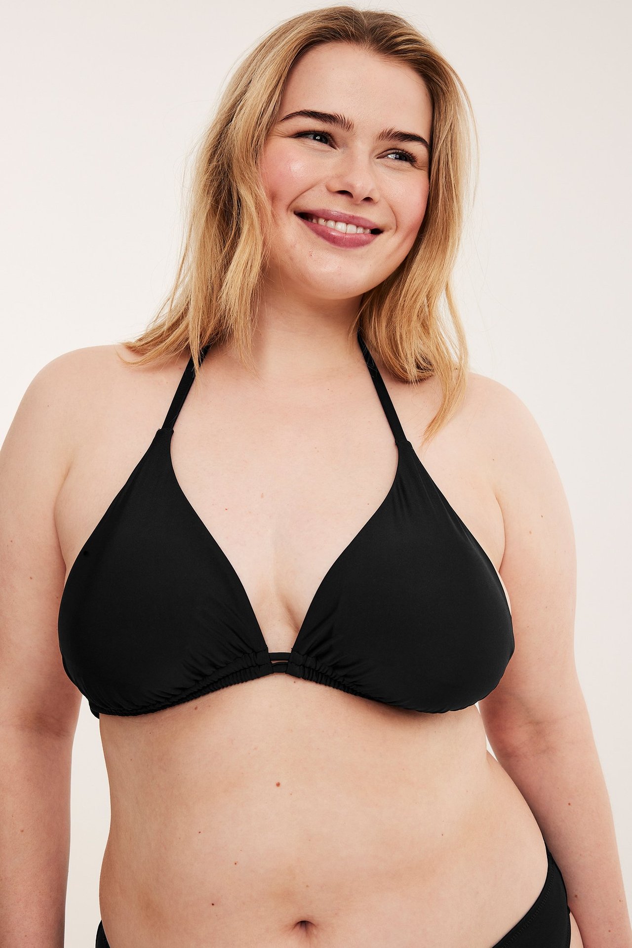 Forfra, smilende kvinne i svart ensfarget trekantbikini-topp og matchende underdel.