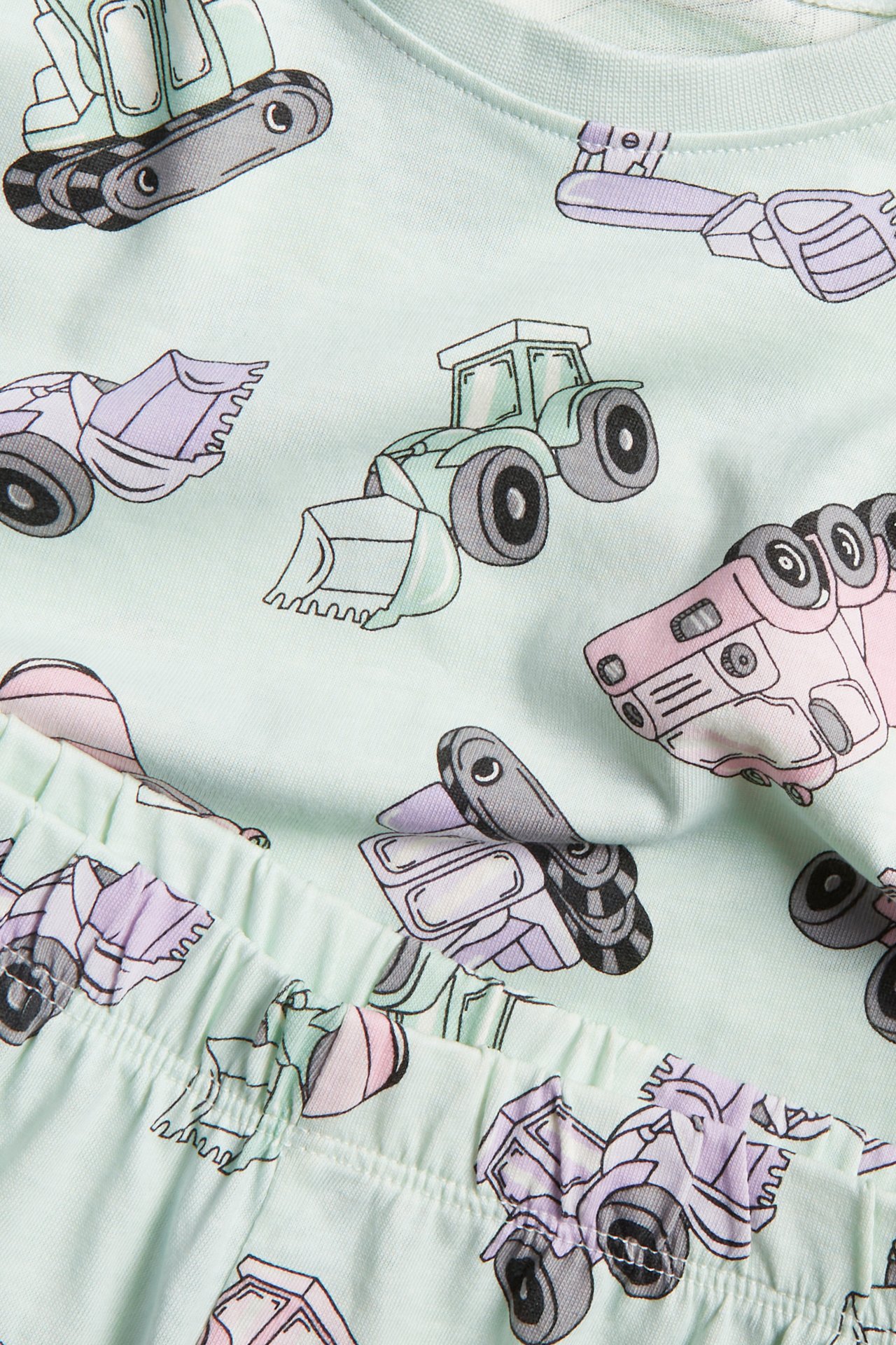 Närbild på en mintgrön pyjamas i bomull för barn med ett heltäckande fordonstryck.