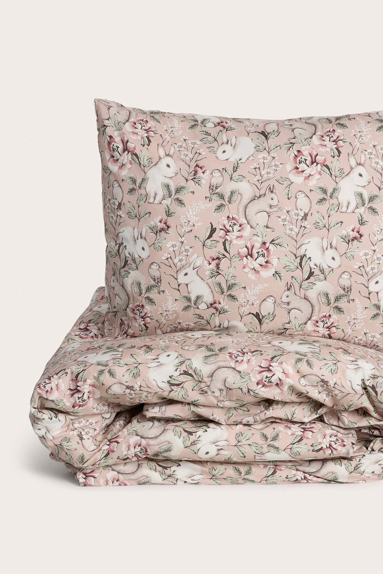 Nærbilde av et rosa bomulls-sengesett med detaljert dyre- og blomstermønster.