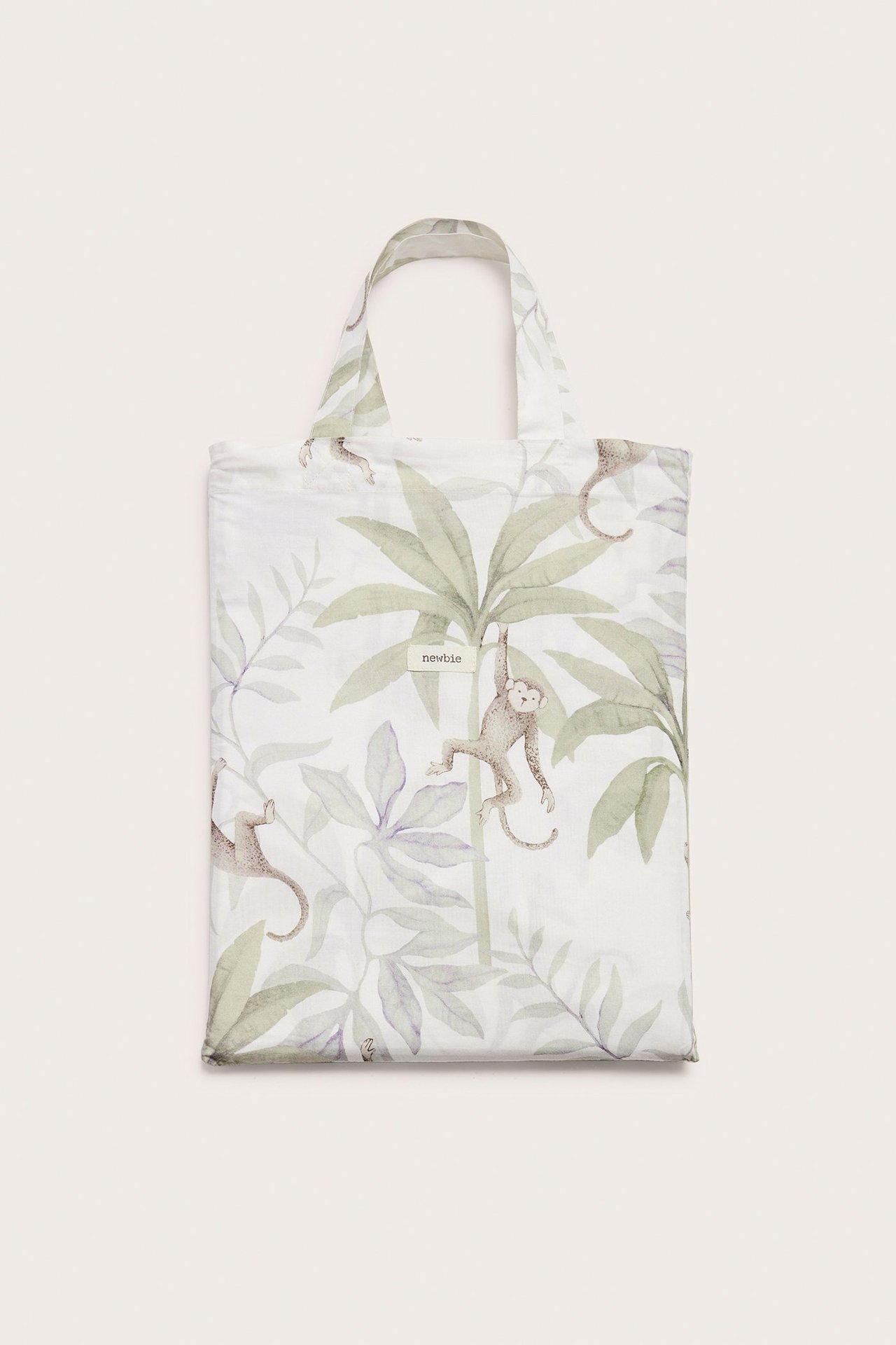 Framifrån: Off-white bomulls-bäddset med djungelmönster av apor och palmblad, vikt som en väska.