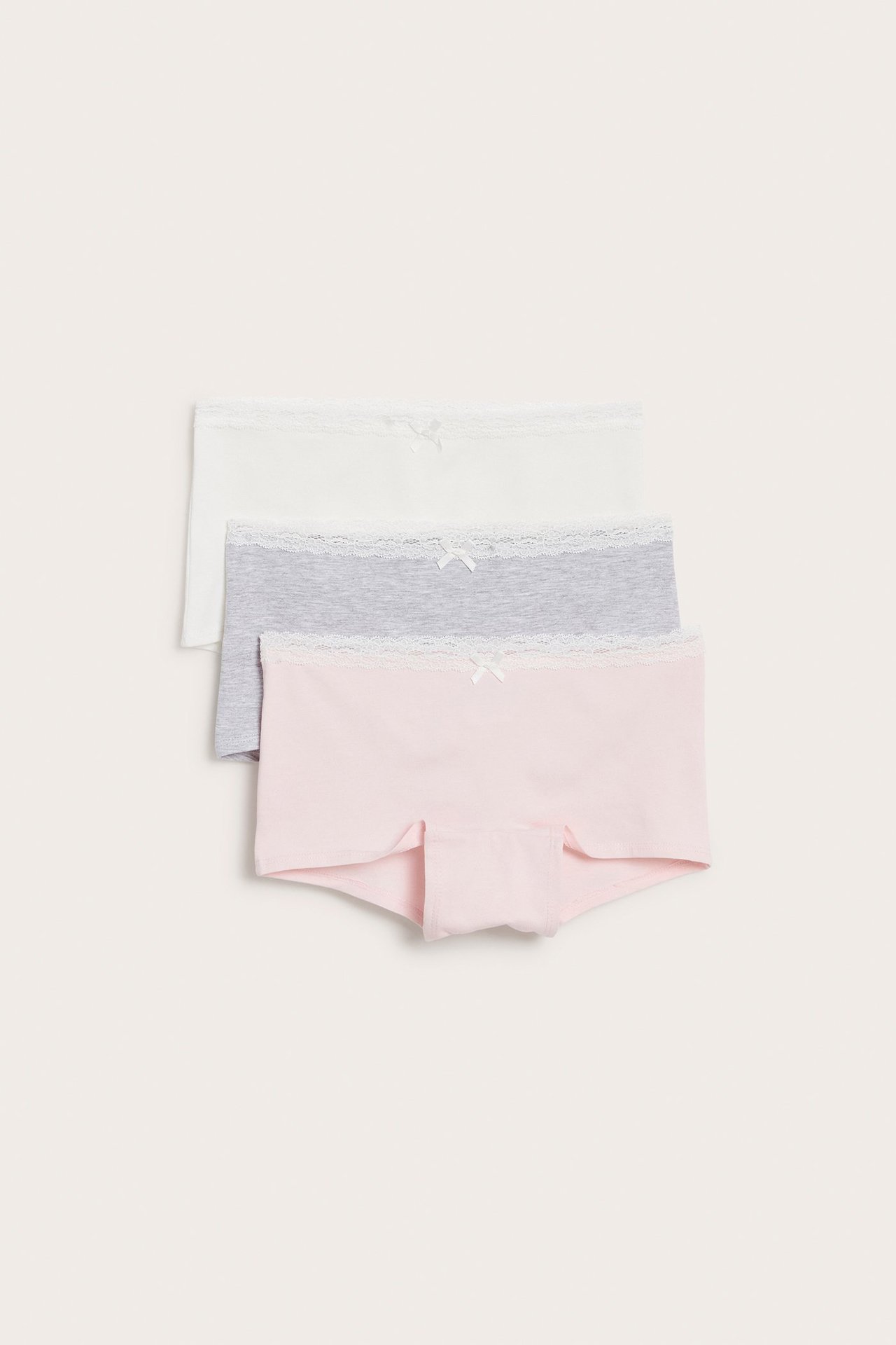 Ylhäältä, kolme lasten puuvillabokseria: vaaleanpunainen, harmaa ja valkoinen, pitsireunalla ja ruseteilla.