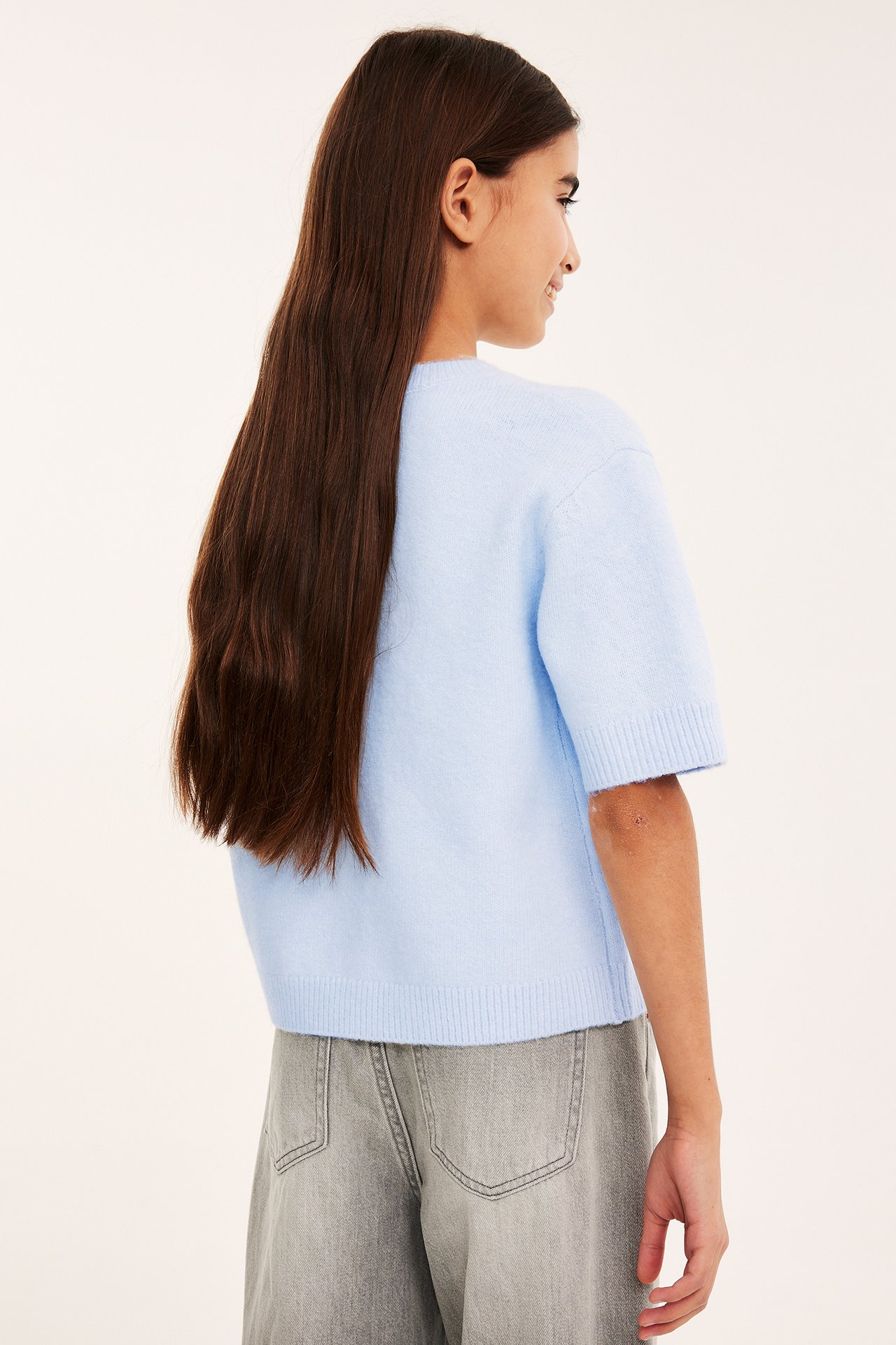 Sidebilde av et barn i en lyseblå kortermet strikket genser og grå jeans.