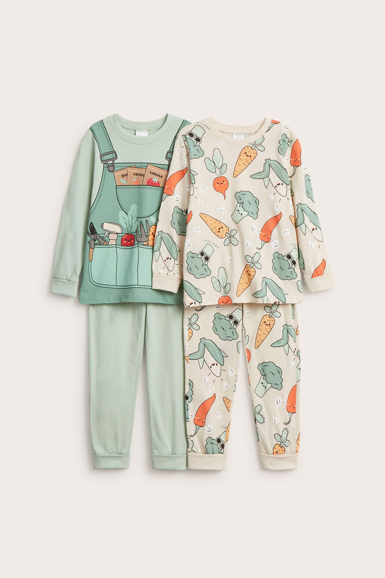 Forfra: To pyjamasett i bomull for barn. Lysegrønn med gartnerprint, off-white med heldekkende grønnsaksmønster.