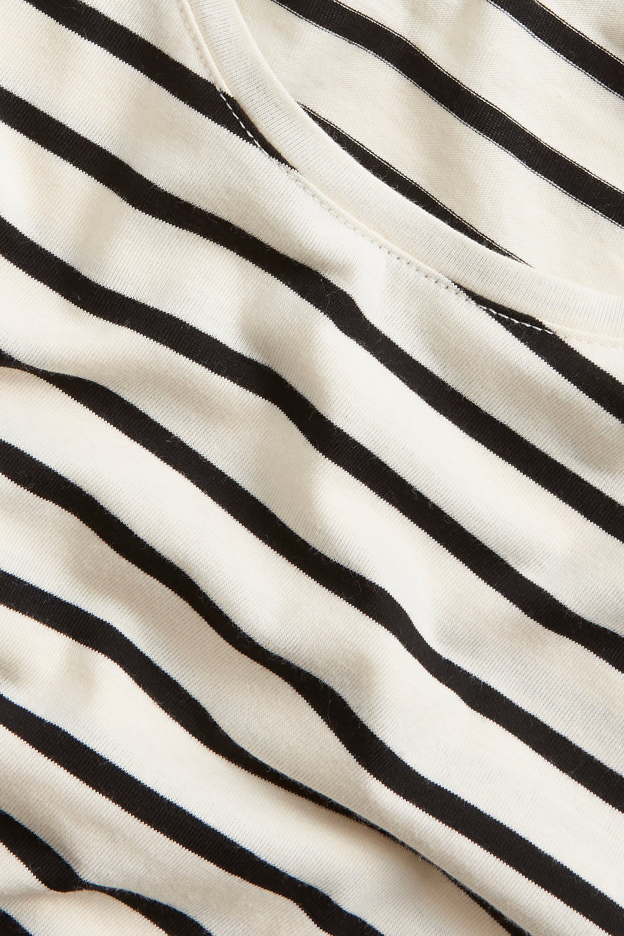 Zbliżenie na bluzkę z długim rękawem w paski off-white i czarne, z okrągłym dekoltem.