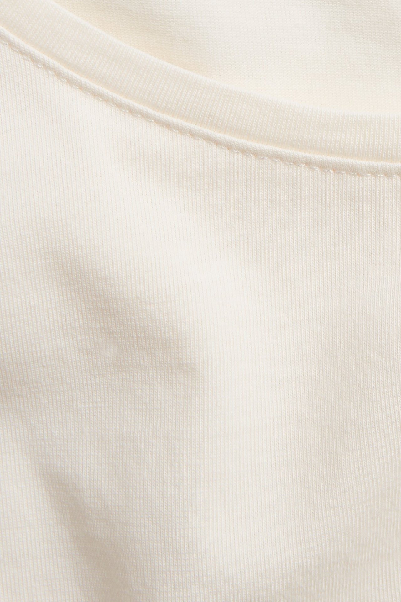 Zbliżenie na kremowy top z długim rękawem, z dekoltem w łódkę i widocznymi szwami.