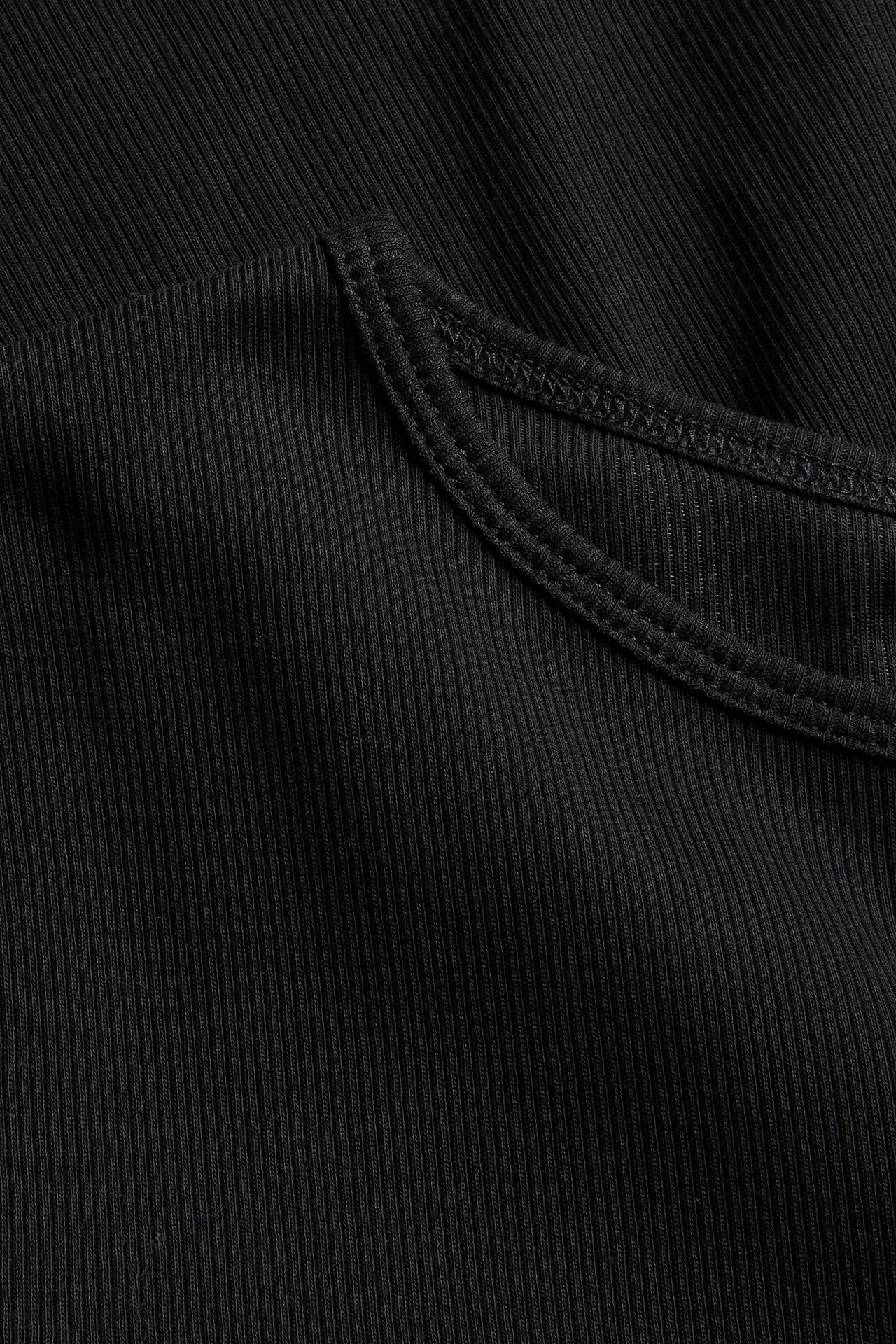Zbliżenie czarnego prążkowanego topu z długim rękawem, ukazujące fakturę materiału i szew.
