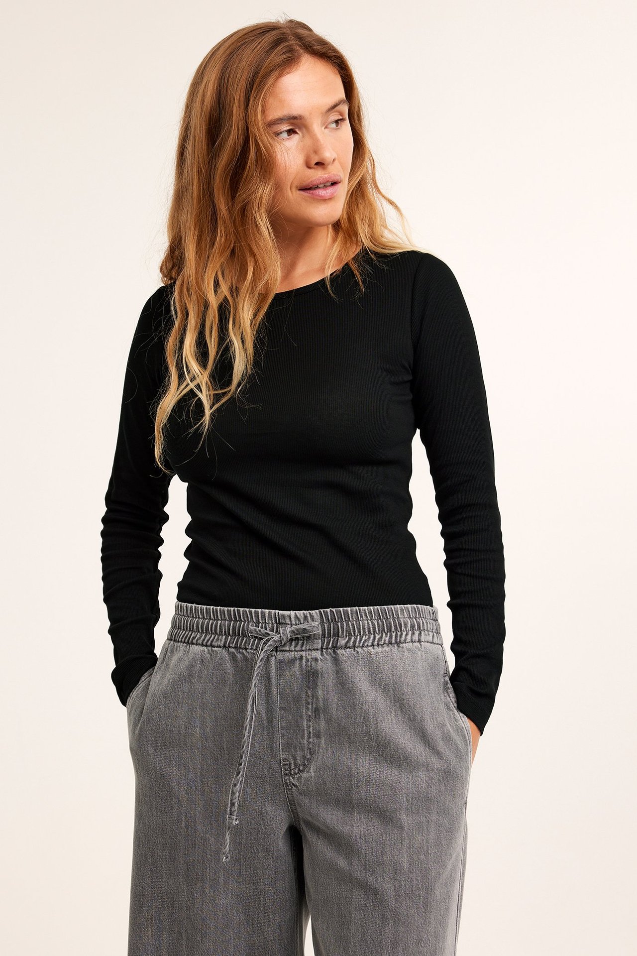 Widok z przodu kobiety w czarnym prążkowanym topie z długim rękawem i szarych szerokich spodniach ze sznurkiem.