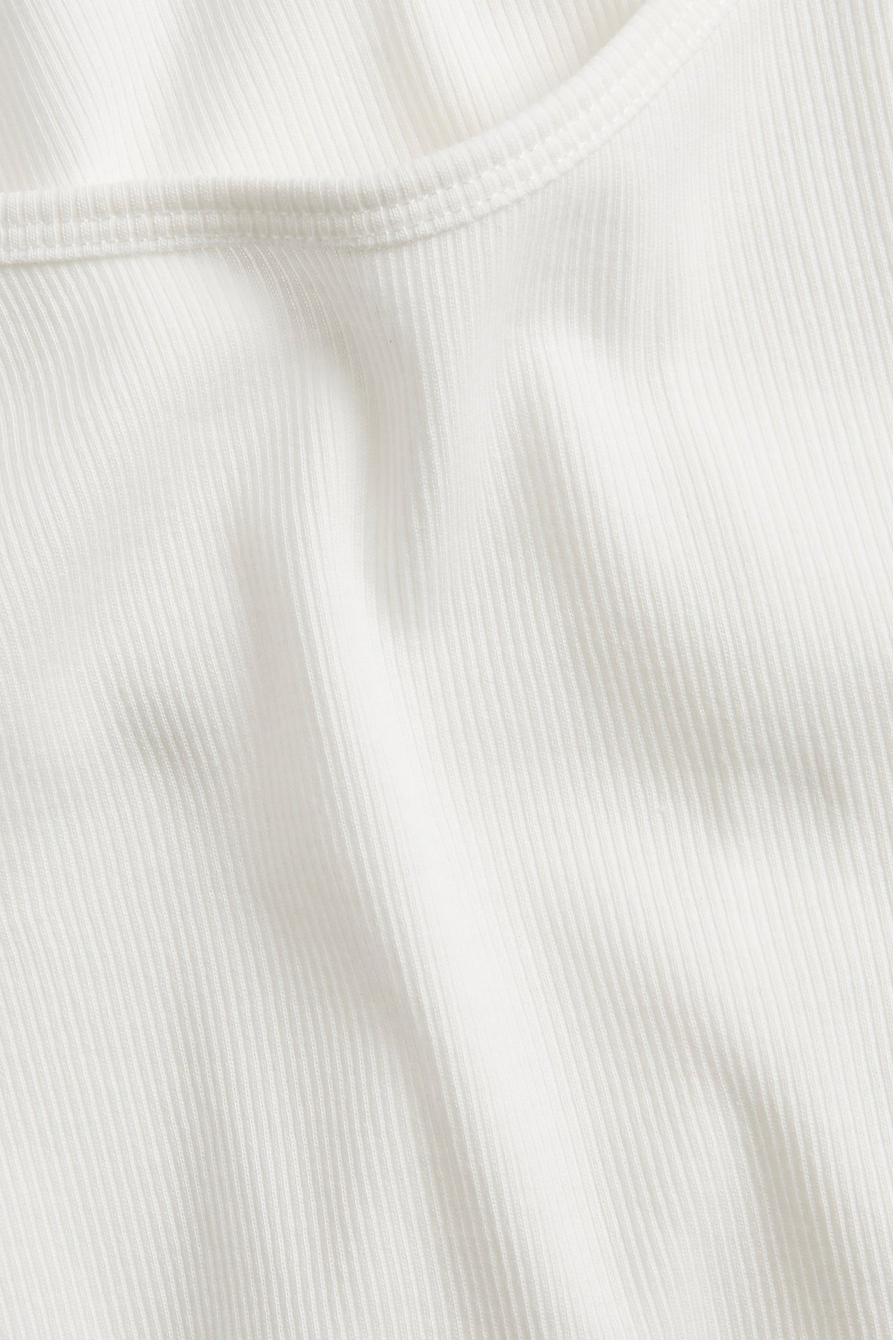 Zbliżenie na kremowy prążkowany top z długim rękawem i okrągłym dekoltem.