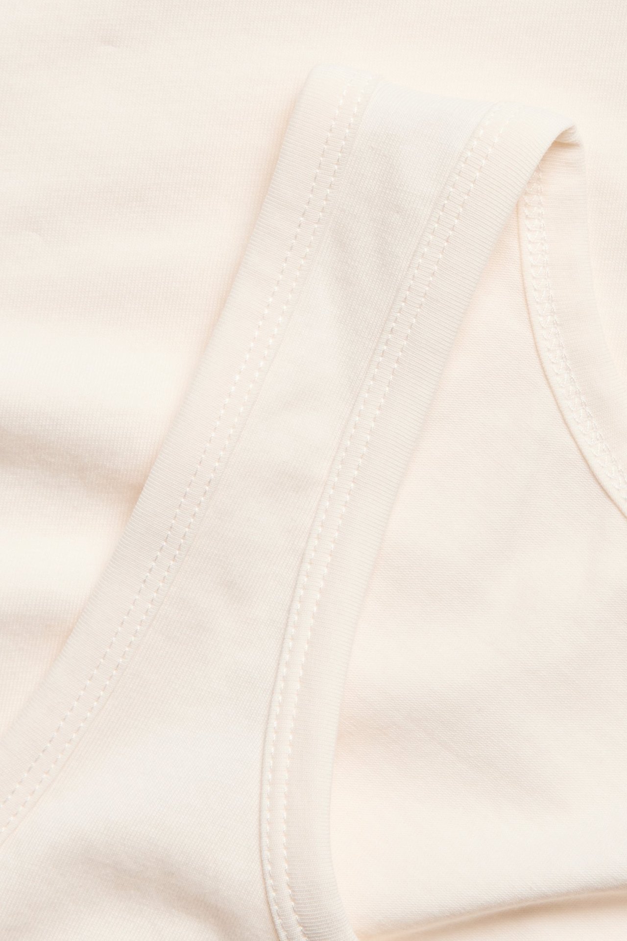 Nærbilde av en offwhite basistopp i bomullsstoff med stretch, som viser sømmer og tekstur.