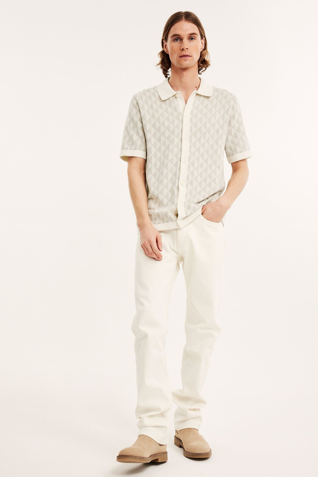 Edestä kuvattu mies yllään vaaleanbeige jacquard-neulepaita, vaaleanbeiget housut ja beiget pistokkaat.