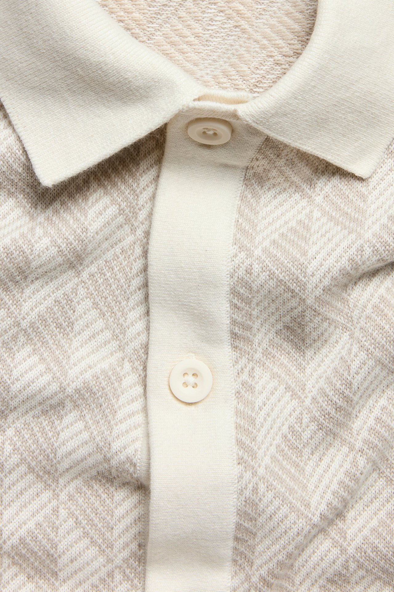 Zbliżenie: Jasnobeżowa dzianinowa koszulka polo z żakardowym wzorem, kremowym kołnierzem i dwoma guzikami.