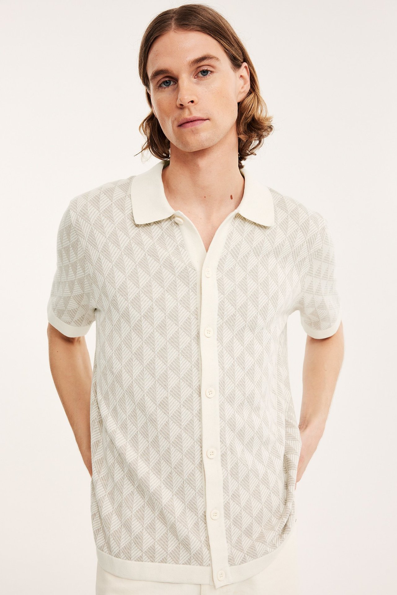 Edestä: mies yllään vaaleanbeige lyhythihainen neulottu pikeepaita, jossa jacquard-kuvio ja napit.