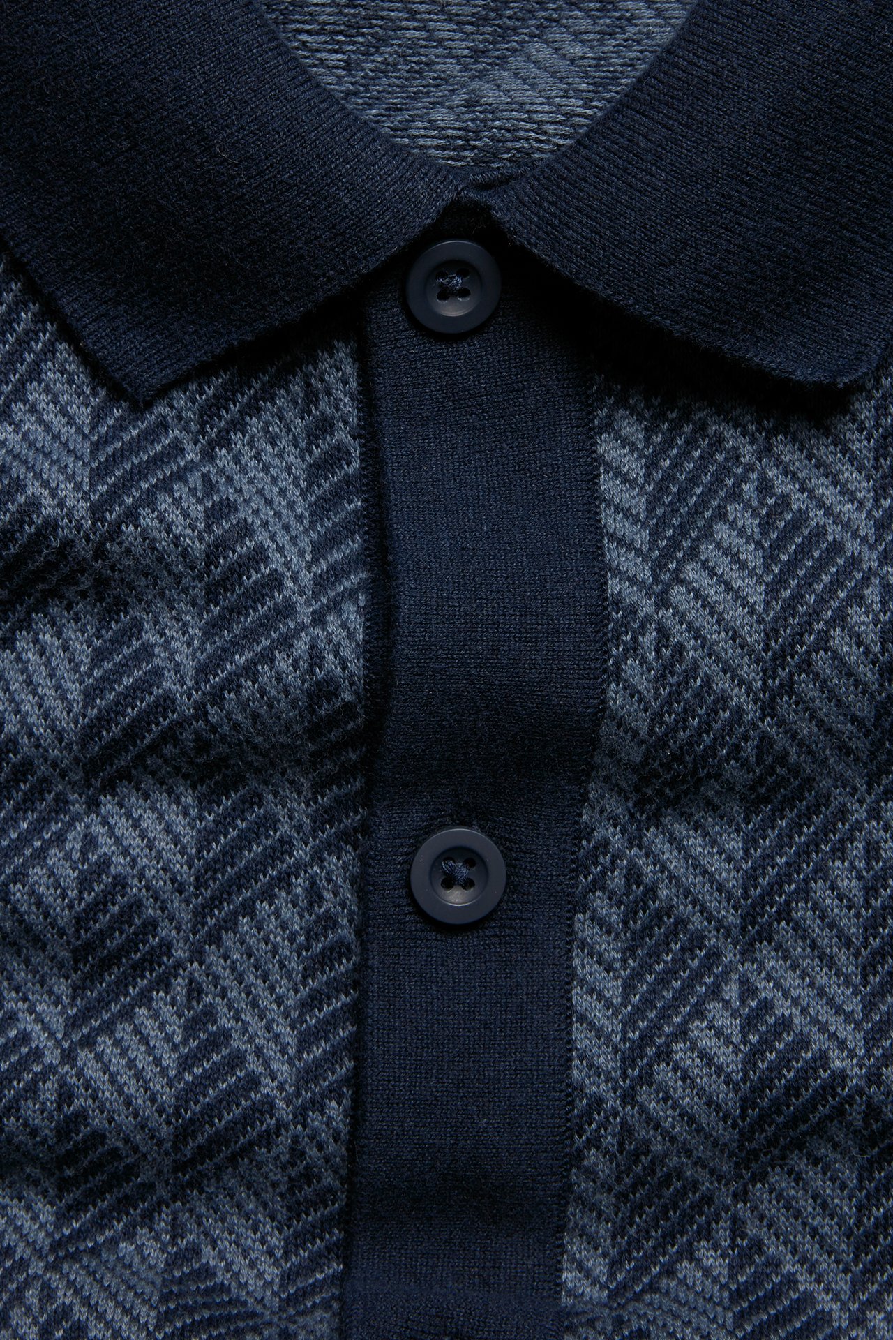 Nærbilde av mørkeblå strikket piké for herre med jacquardmønster og knapper foran.