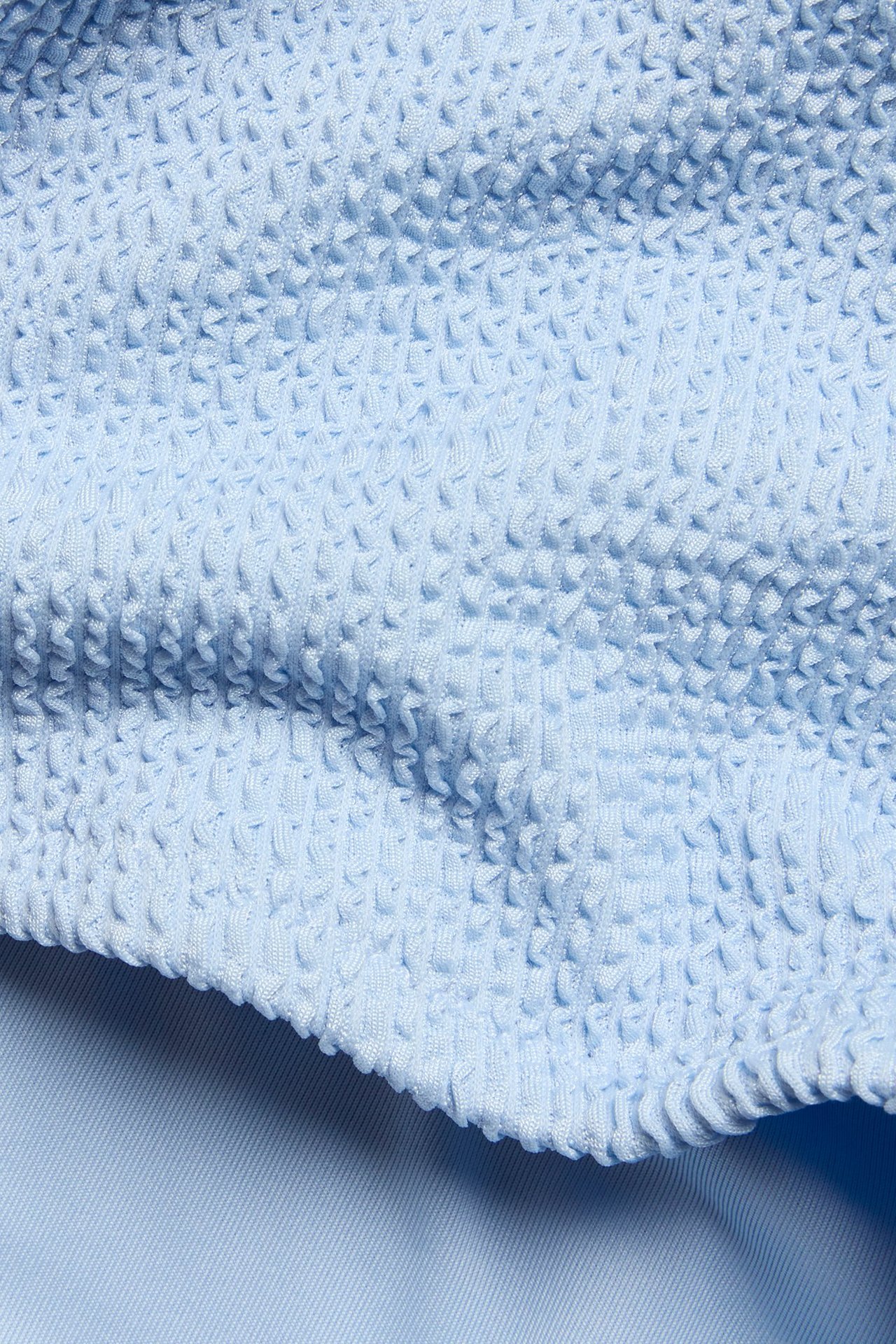 Zbliżenie na jasnoniebieski, teksturowany materiał wysokich szortów kąpielowych.