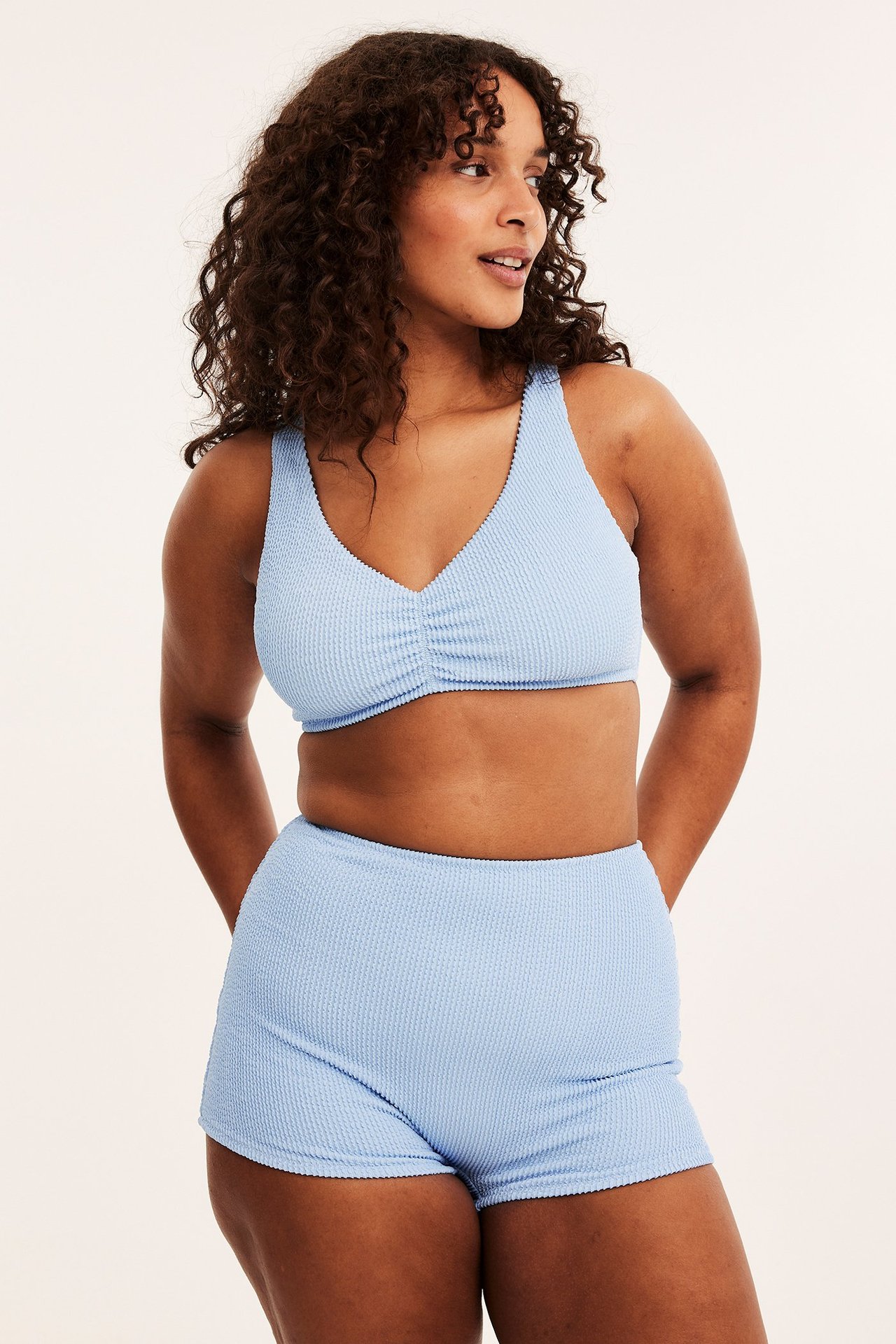 Widok z przodu: kobieta w jasnoniebieskich, teksturowanych wysokich szortach bikini i pasującym topie bikini.
