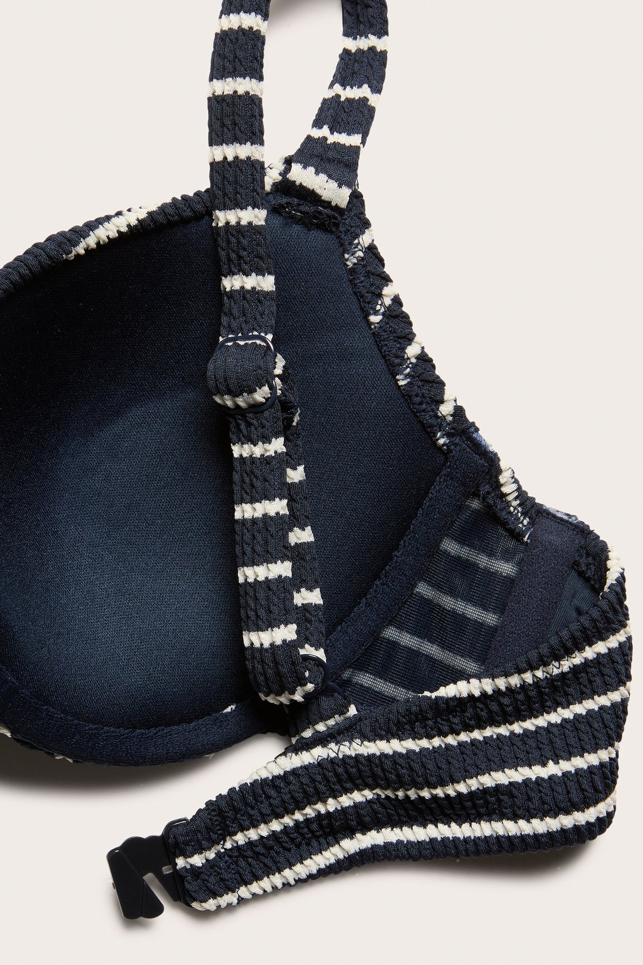 Zbliżenie na granatowy i biały, prążkowany biustonosz bikini z regulowanymi ramiączkami i czarnym zapięciem.