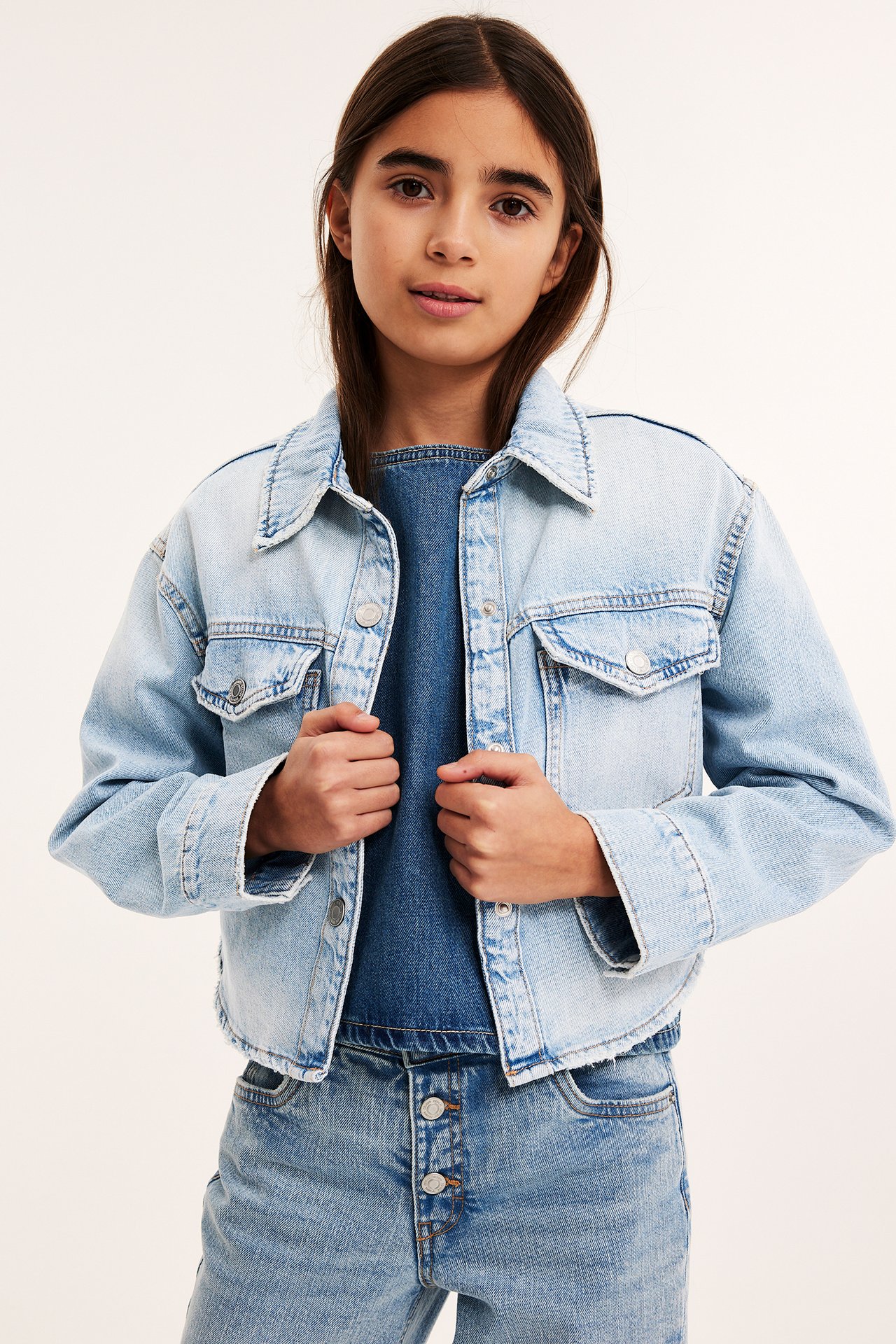 Edestäpäin, lapsi yllään vaalea denim-laatikkomainen takki, tumma denim-toppi ja vaaleat farkut.