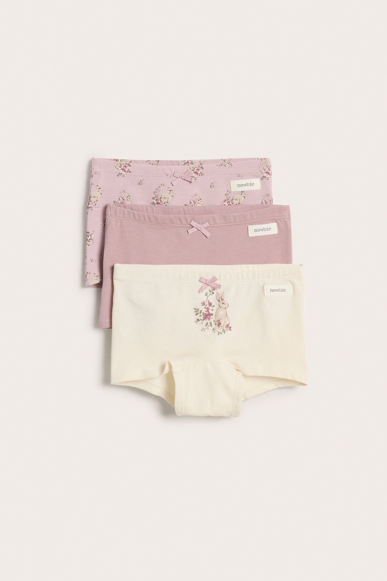 Frontvisning av tre barne-bomullsboxershorts med sløyfer: offwhite kanin, ensfarget lys lilla, rosa blomstret.