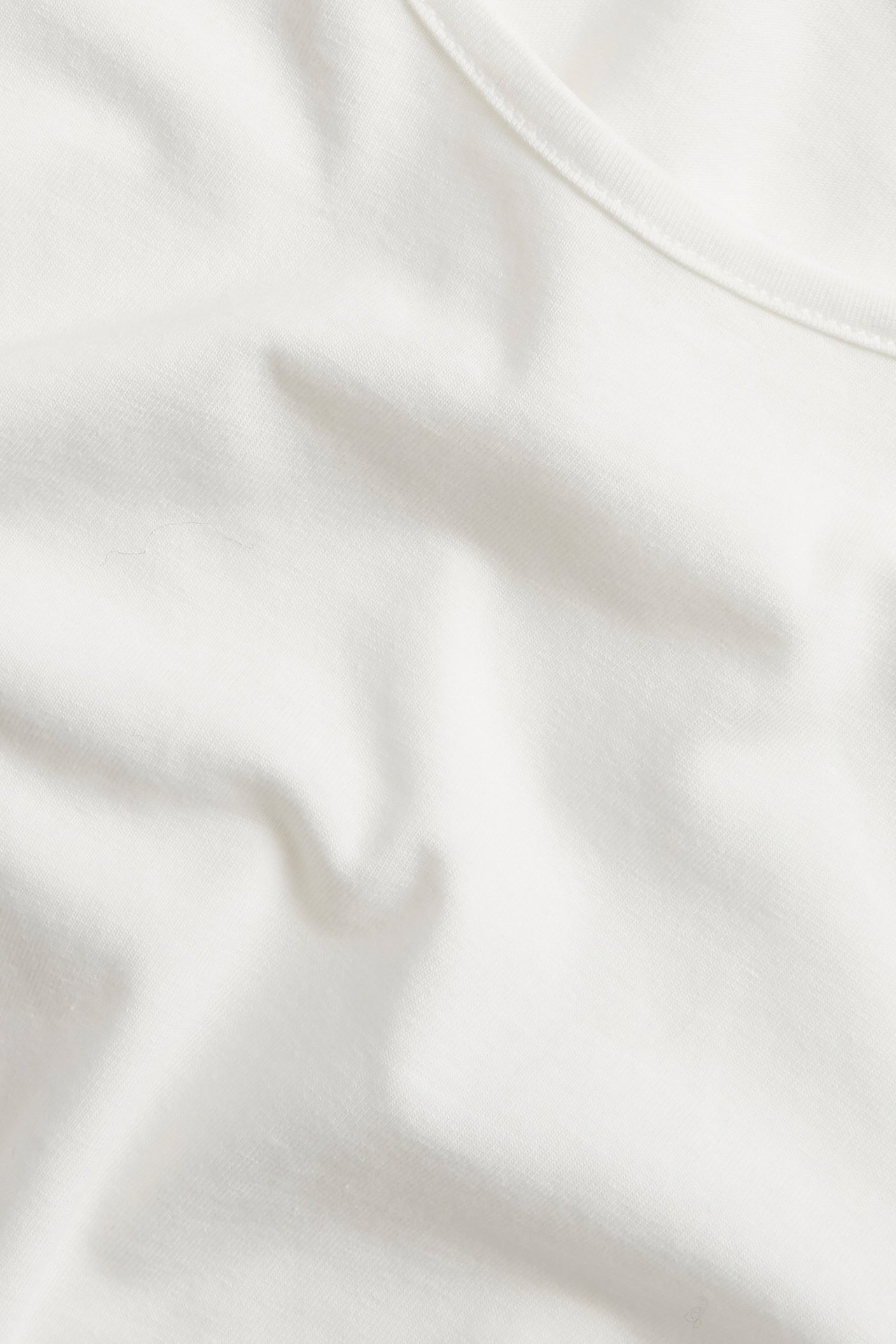 Närbild av en enfärgad offwhite långärmad topp i bomullstrikå med synlig halsringningssöm.