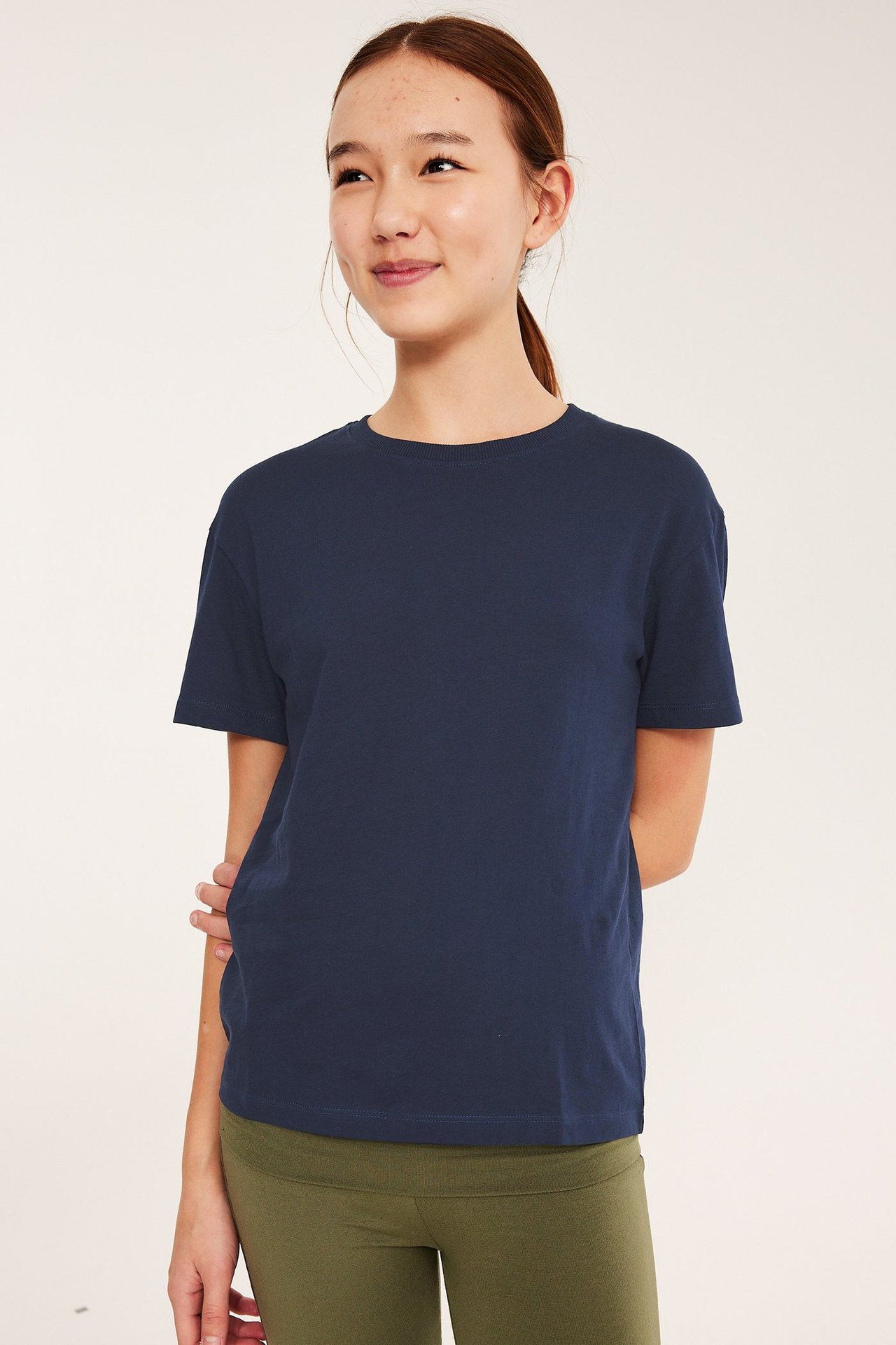 Frontbilde av et barn i en mørkeblå ensfarget bomulls-T-skjorte og olivengrønne leggings.