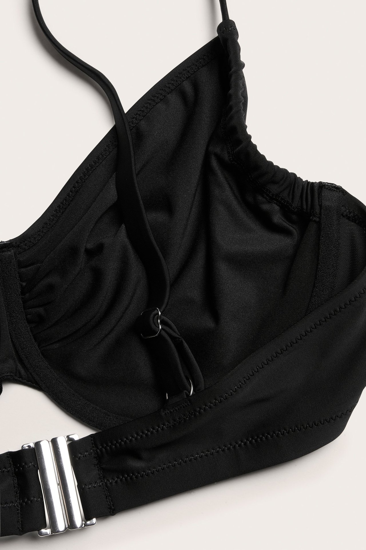 Zbliżenie czarnego, nieusztywnianego biustonosza bikini z fiszbinami, regulowanymi ramiączkami i srebrnym zapięciem.