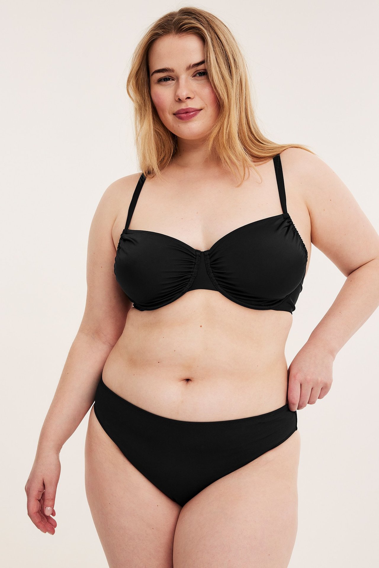 Widok z przodu: kobieta w czarnym biustonoszu bikini na fiszbinach z marszczonymi miseczkami i pasujących majtkach.
