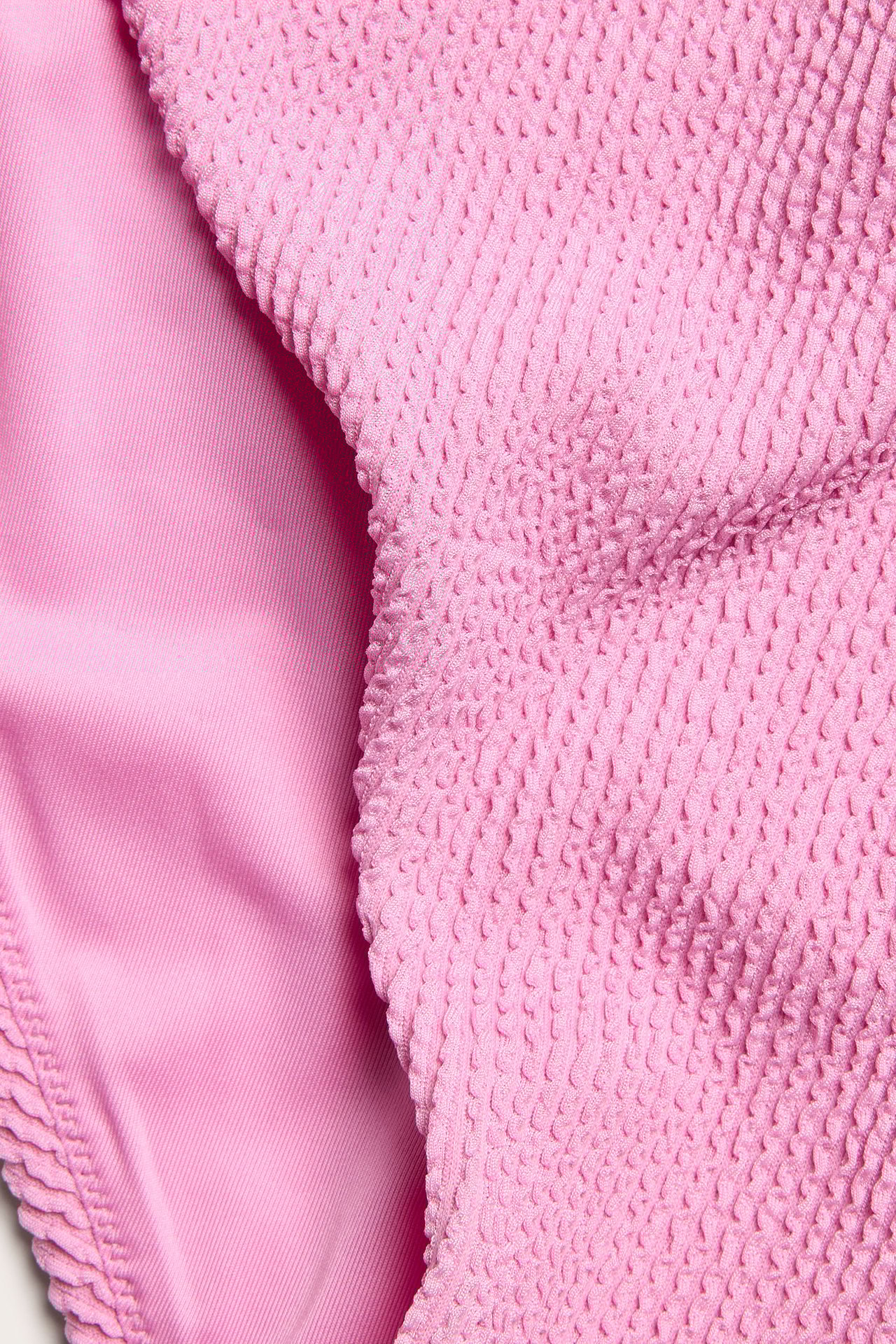 Zbliżenie jasnoróżowych, teksturowanych majtek bikini z gładką podszewką.