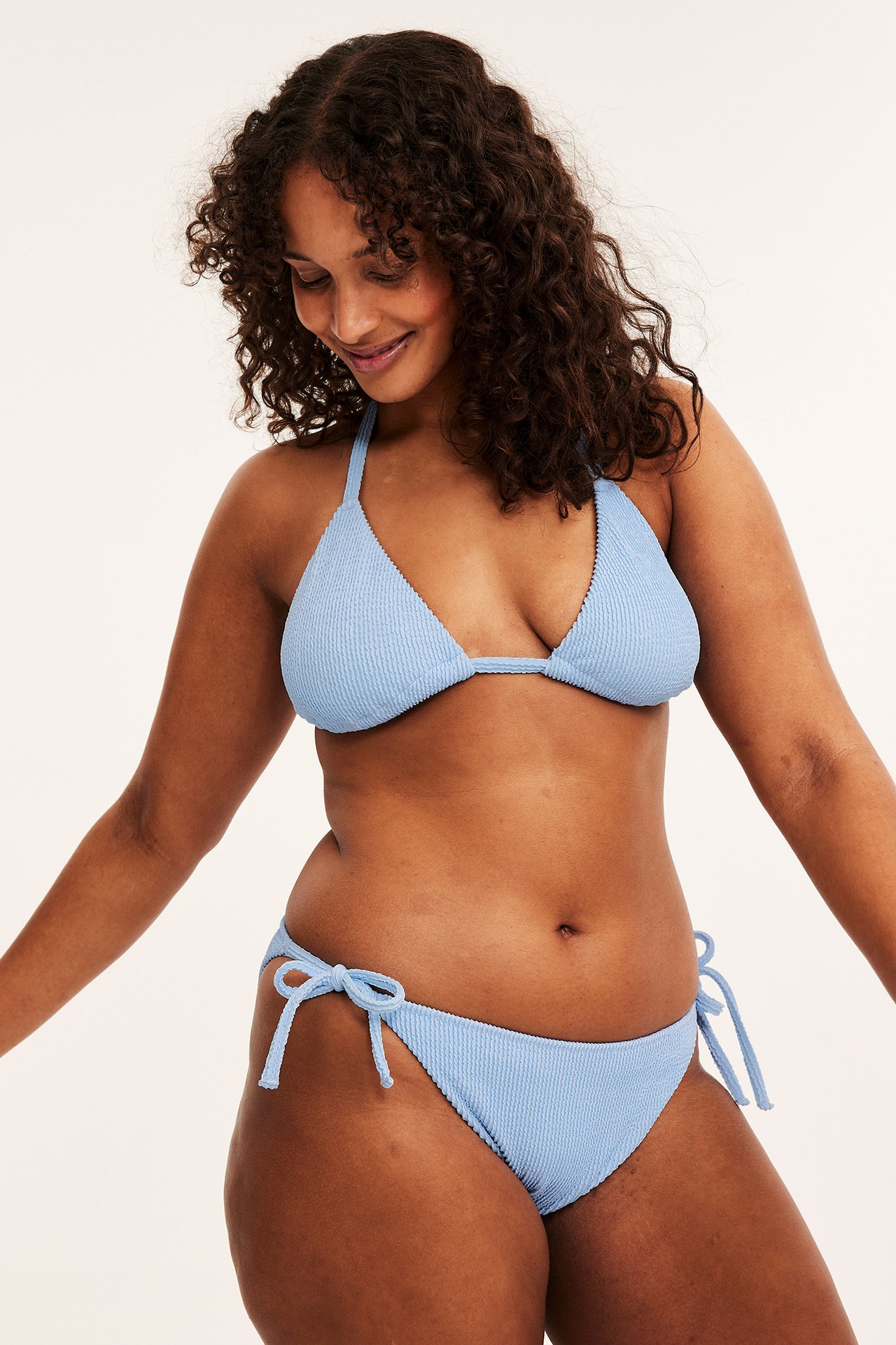 Edestäpäin, nainen yllään vaaleansiniset kuvioidut Brazilian-bikinihousut solmimisnauhoilla ja yhteensopiva kolmio-bikinitoppi.