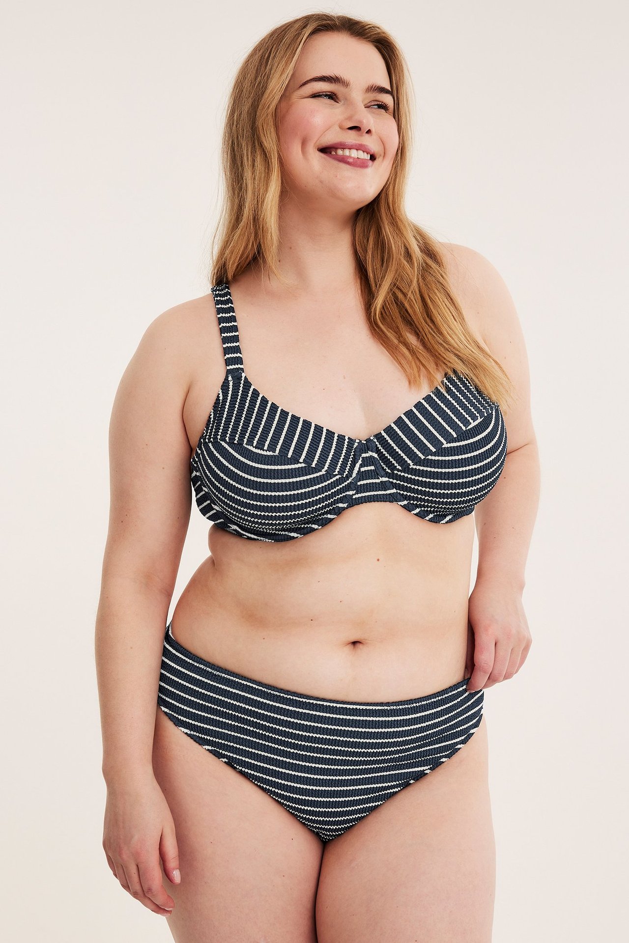 Forfra, smilende kvinne i mørkeblå stripet bikinitopp og matchende underdel.