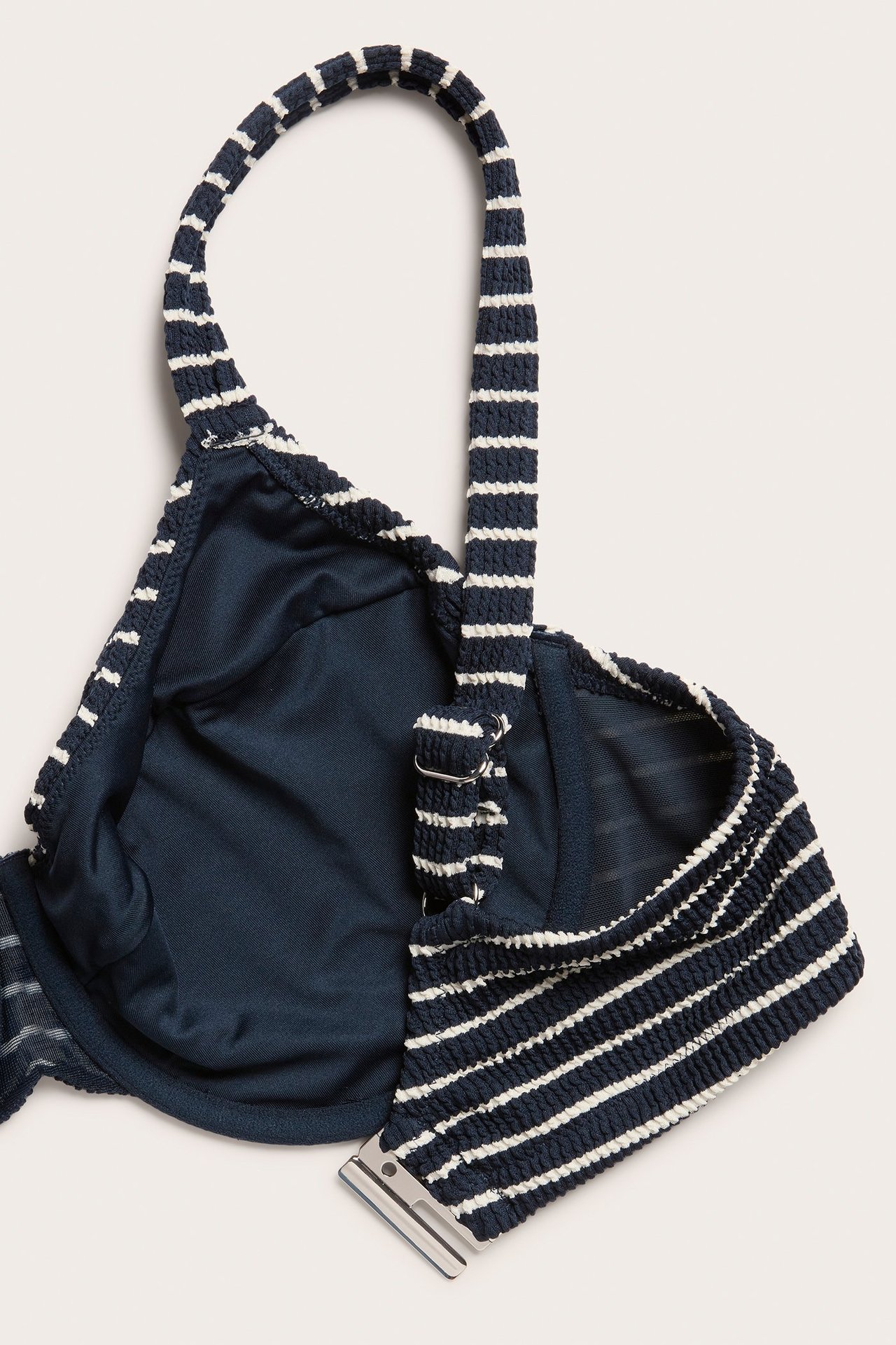 Zbliżenie na granatowy i biały biustonosz bikini w paski z regulowanymi ramiączkami i metalowym zapięciem.