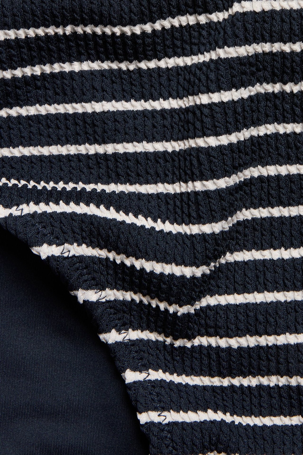 Zbliżenie na granatowo-biały, prążkowany, teksturowany materiał majtek kąpielowych.