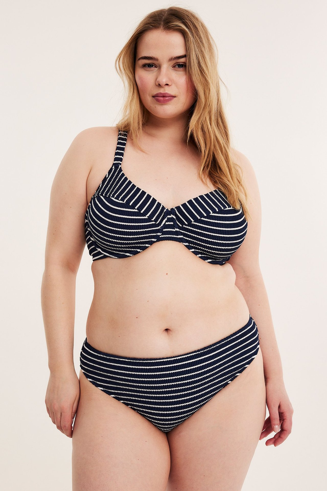 Kobieta w granatowo-białym, pasiastym bikini z wysokim wycięciem i pasującym topie, widok z przodu.