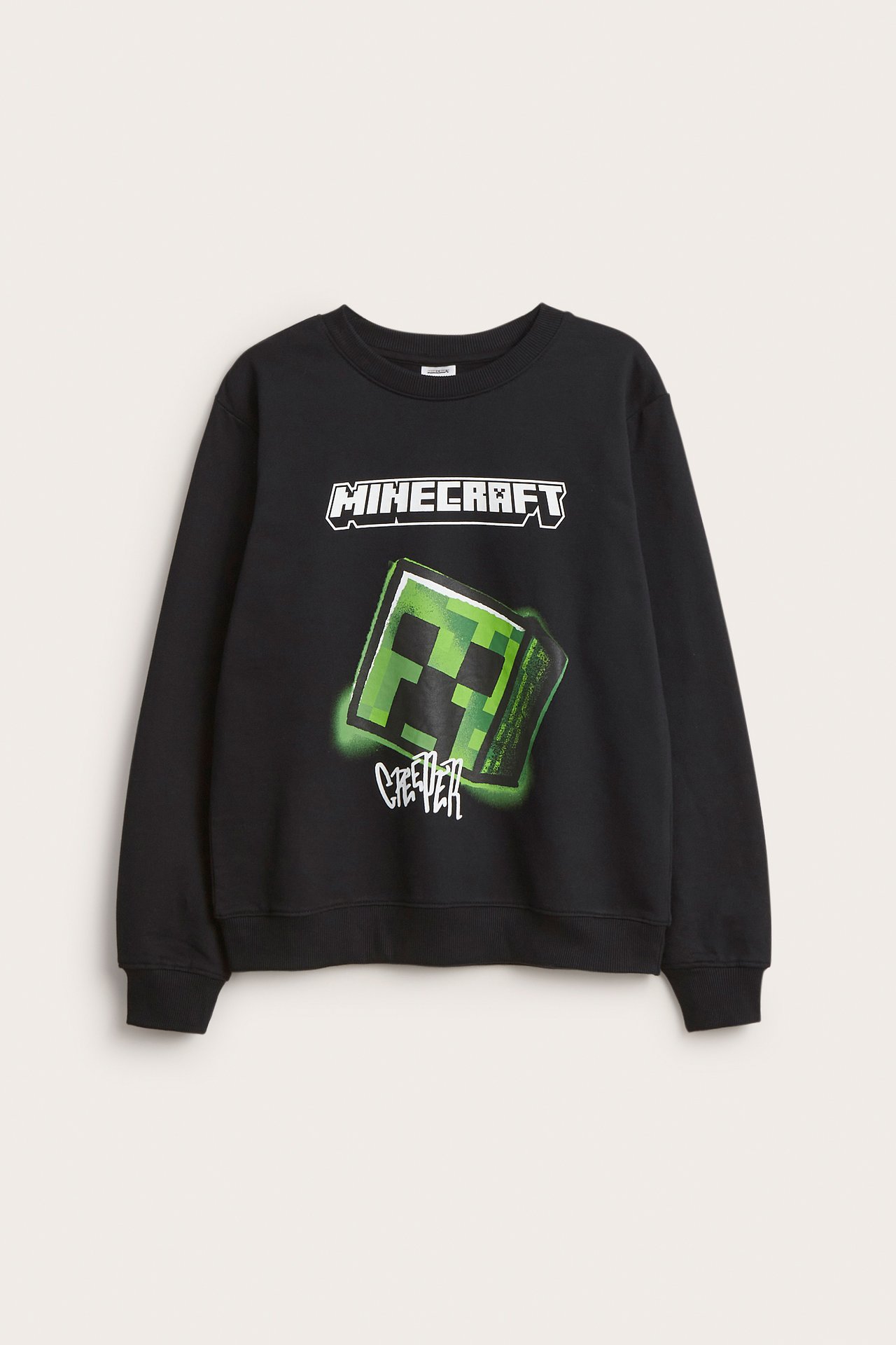 Edestä näkymä lasten mustasta puuvillapaidasta, jossa on suuri vihreä Minecraft Creeper -painatus ja teksti.