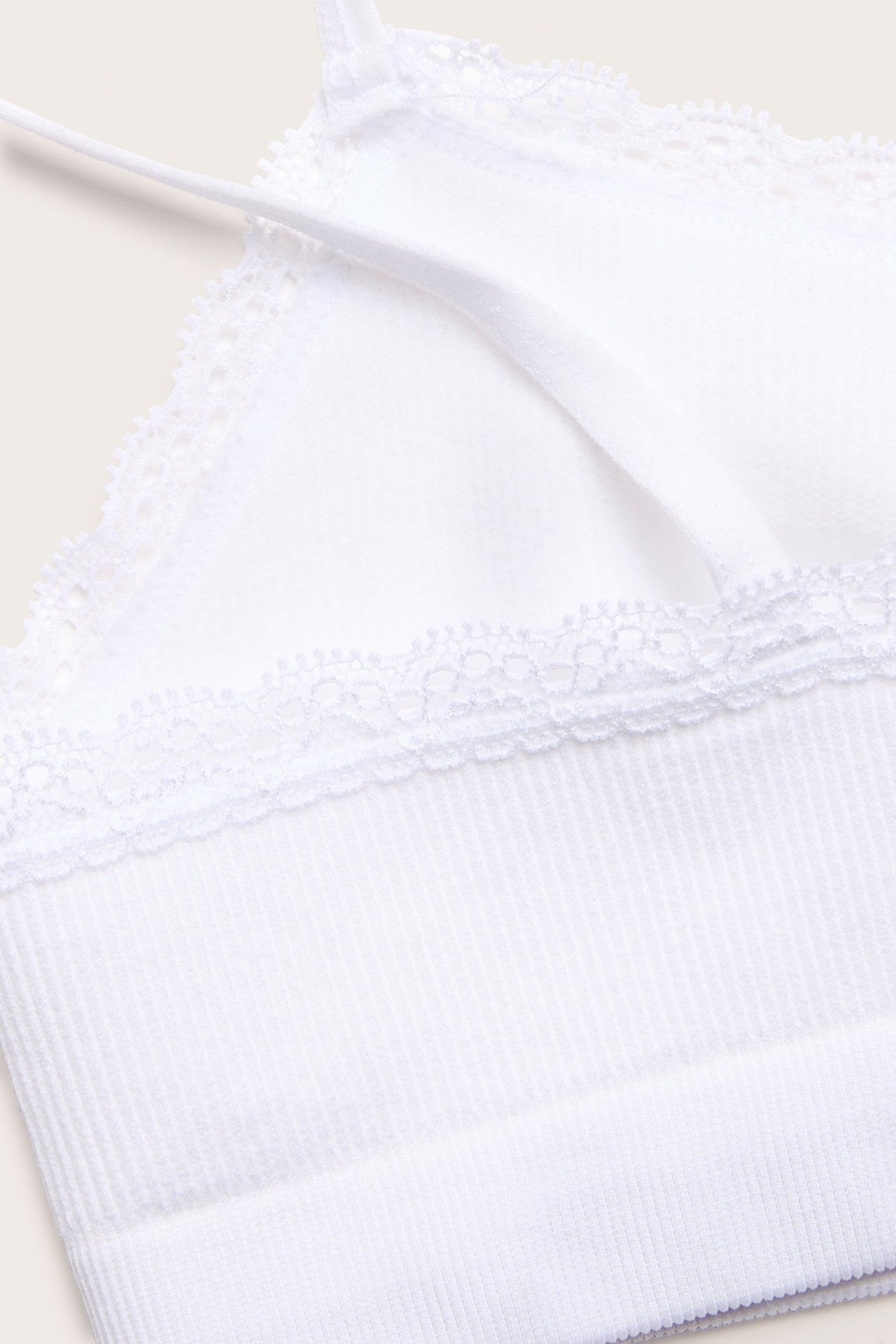 Zbliżenie białego, bezszwowego, prążkowanego topu z cienkimi ramiączkami i delikatną koronkową lamówką.