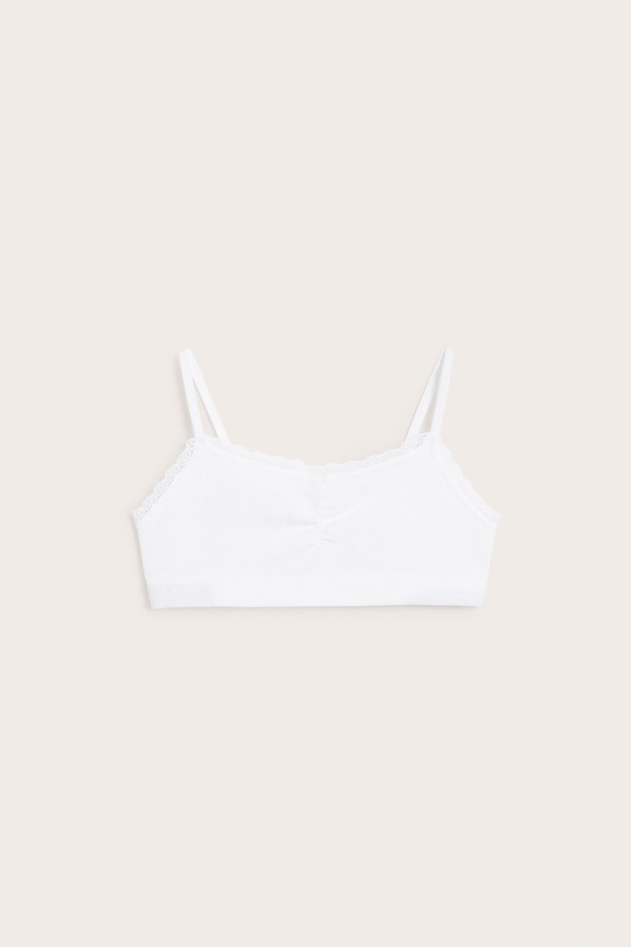 Edestä: lasten valkoinen saumaton ribbineuleinen bralette-toppi ohuilla olkaimilla ja pitsireunalla.